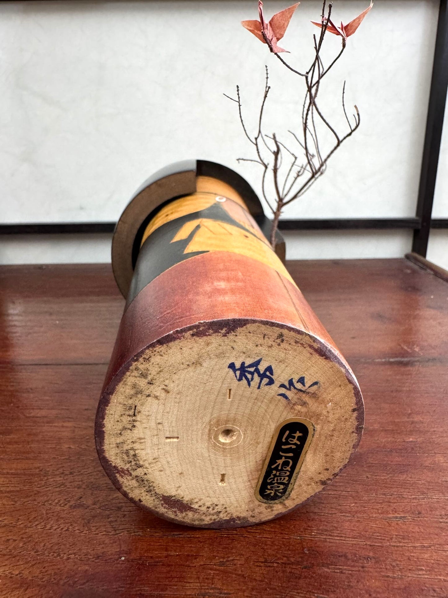 Kokeshi vintage Shinonome de Kisaku avec kimono sculpté en relief et coiffure noire, vu de dessous la signature de l'artisan