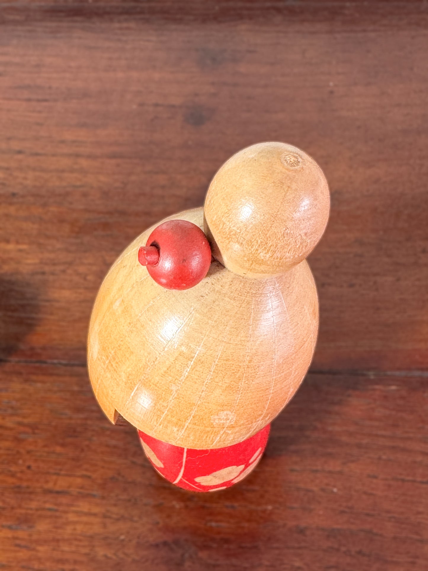 kokeshi, poupée japonaise en bois de Sato Suigai, avec tête penchée, visage souriant et kimono rouge avec fleurs de cerisier gravées, vu de dessus