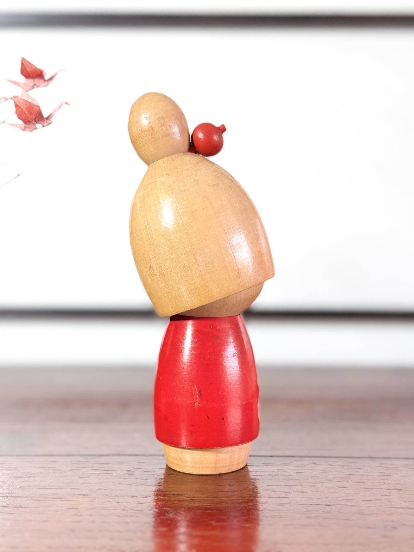 kokeshi, poupée japonaise en bois de Sato Suigai, avec tête penchée, visage souriant et kimono rouge avec fleurs de cerisier gravées, vu de 3/4