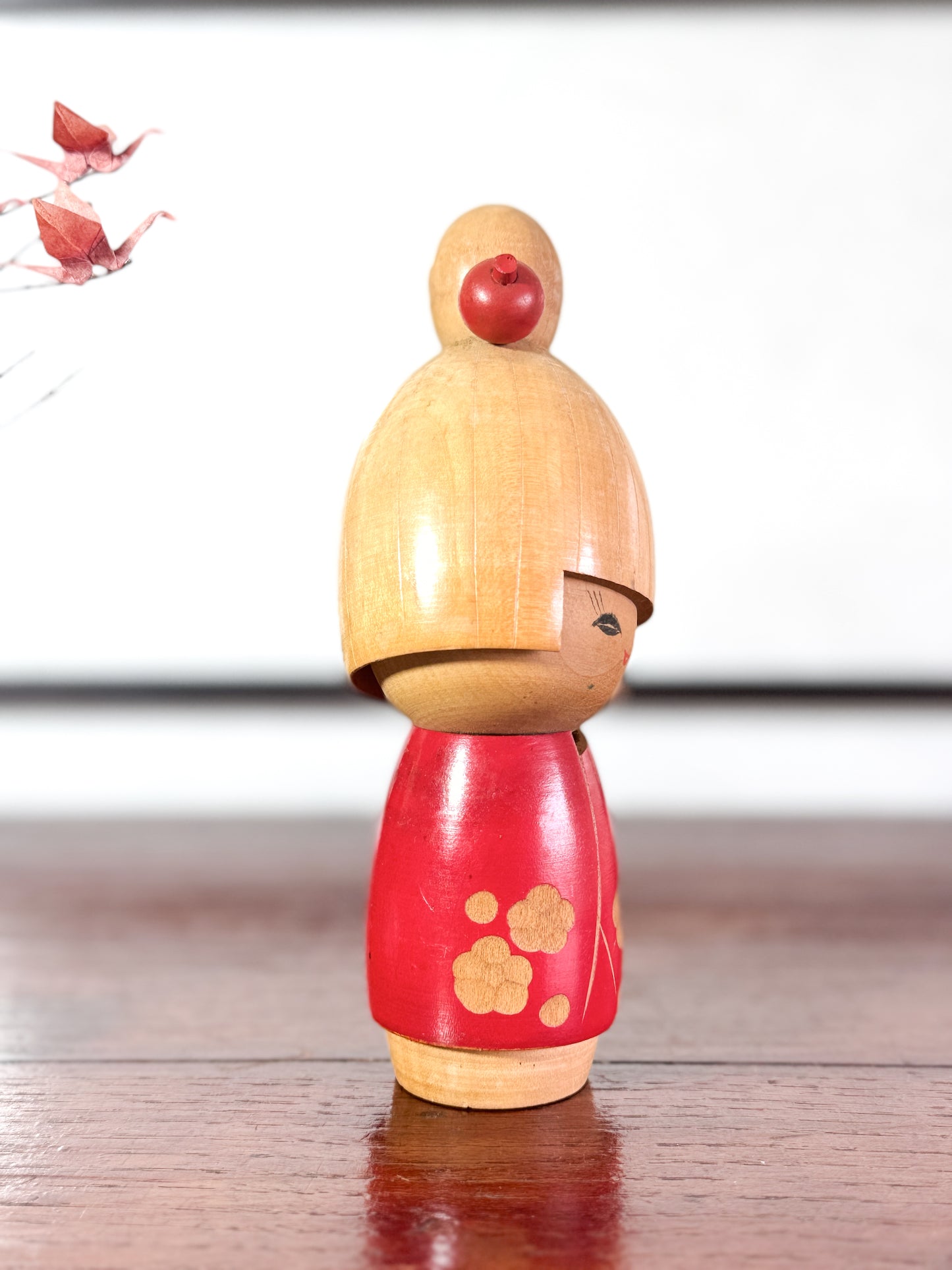 kokeshi, poupée japonaise en bois de Sato Suigai, avec tête penchée, visage souriant et kimono rouge avec fleurs de cerisier gravées, profil droit