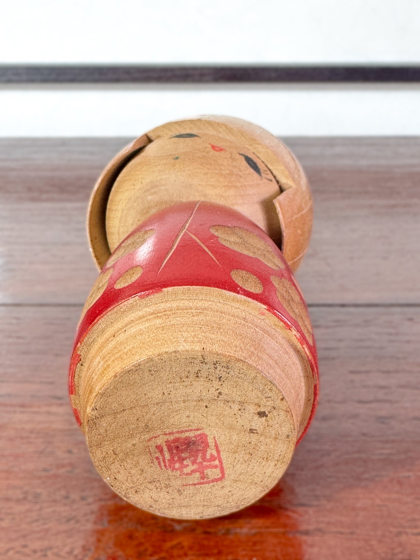 kokeshi, poupée japonaise en bois de Sato Suigai, avec tête penchée, visage souriant et kimono rouge avec fleurs de cerisier gravées, la signature au dessous