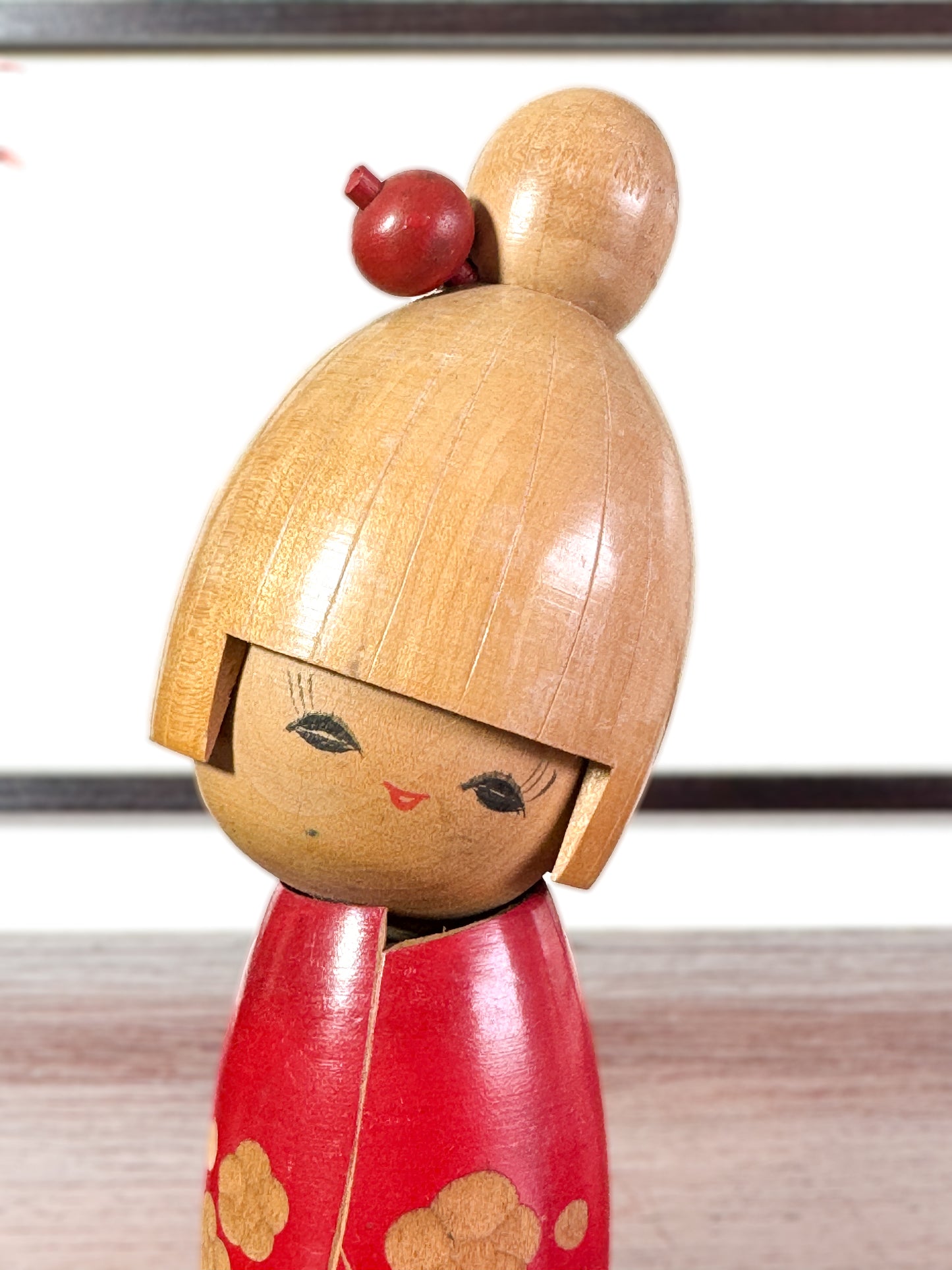 kokeshi, poupée japonaise en bois de Sato Suigai, avec tête penchée, visage souriant et kimono rouge avec fleurs de cerisier gravées, gros plan sur le visage.