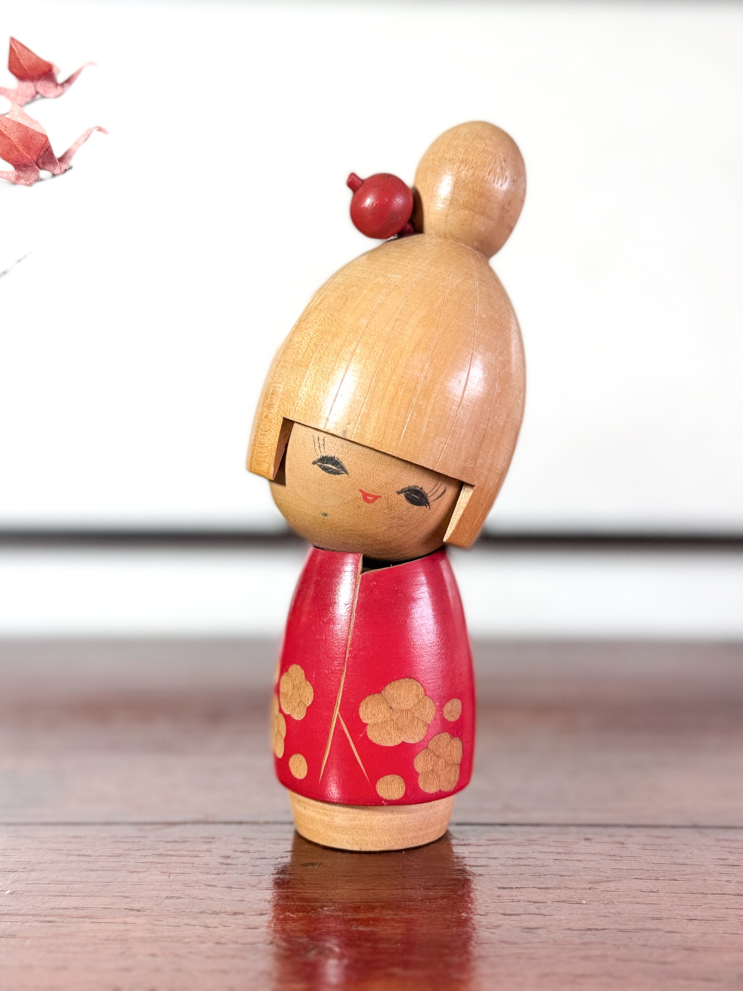 kokeshi, poupée japonaise en bois de Sato Suigai, avec tête penchée, visage souriant et kimono rouge avec fleurs de cerisier gravées.