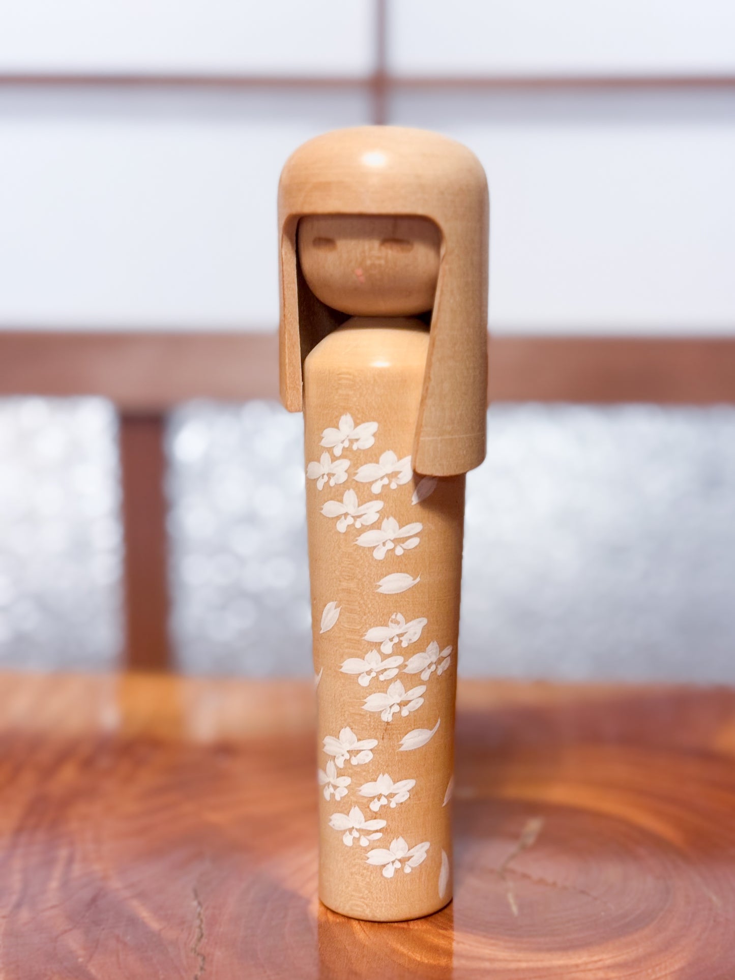kokeshi de Miyashita Mihutsu en bois naturel avec fleurs blanches peintes et longue chevelure, vu de 3/4 gauche