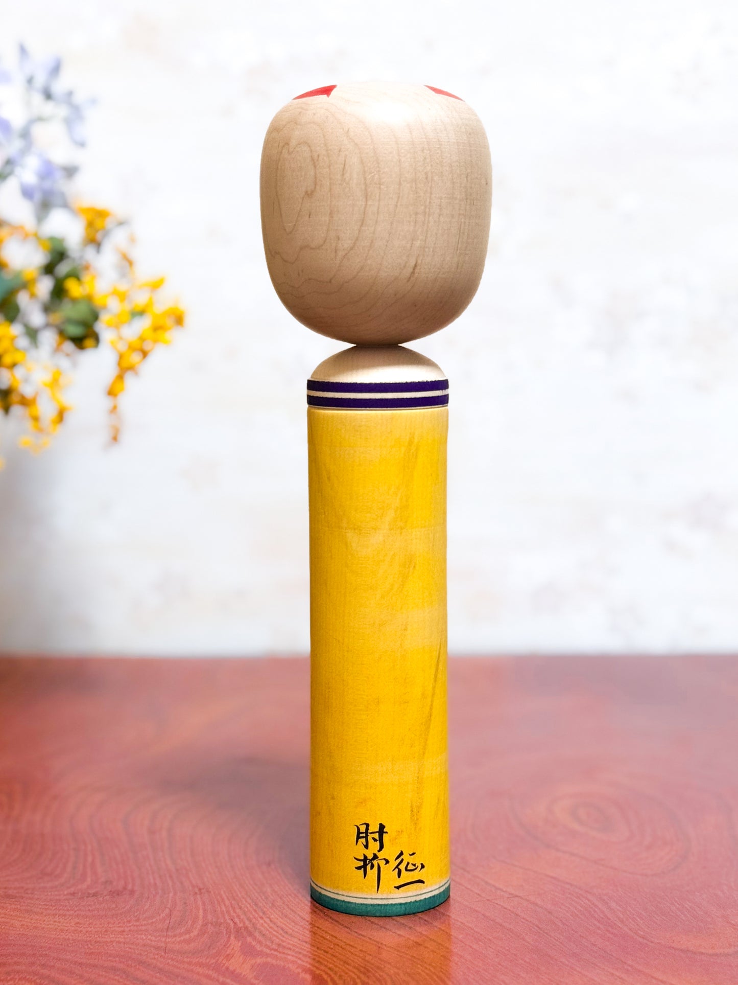 kokeshi traditionelle motif chrysanthème rouge sur fond jaune, visage souriant, vu de dos avec la signature de l'artisan