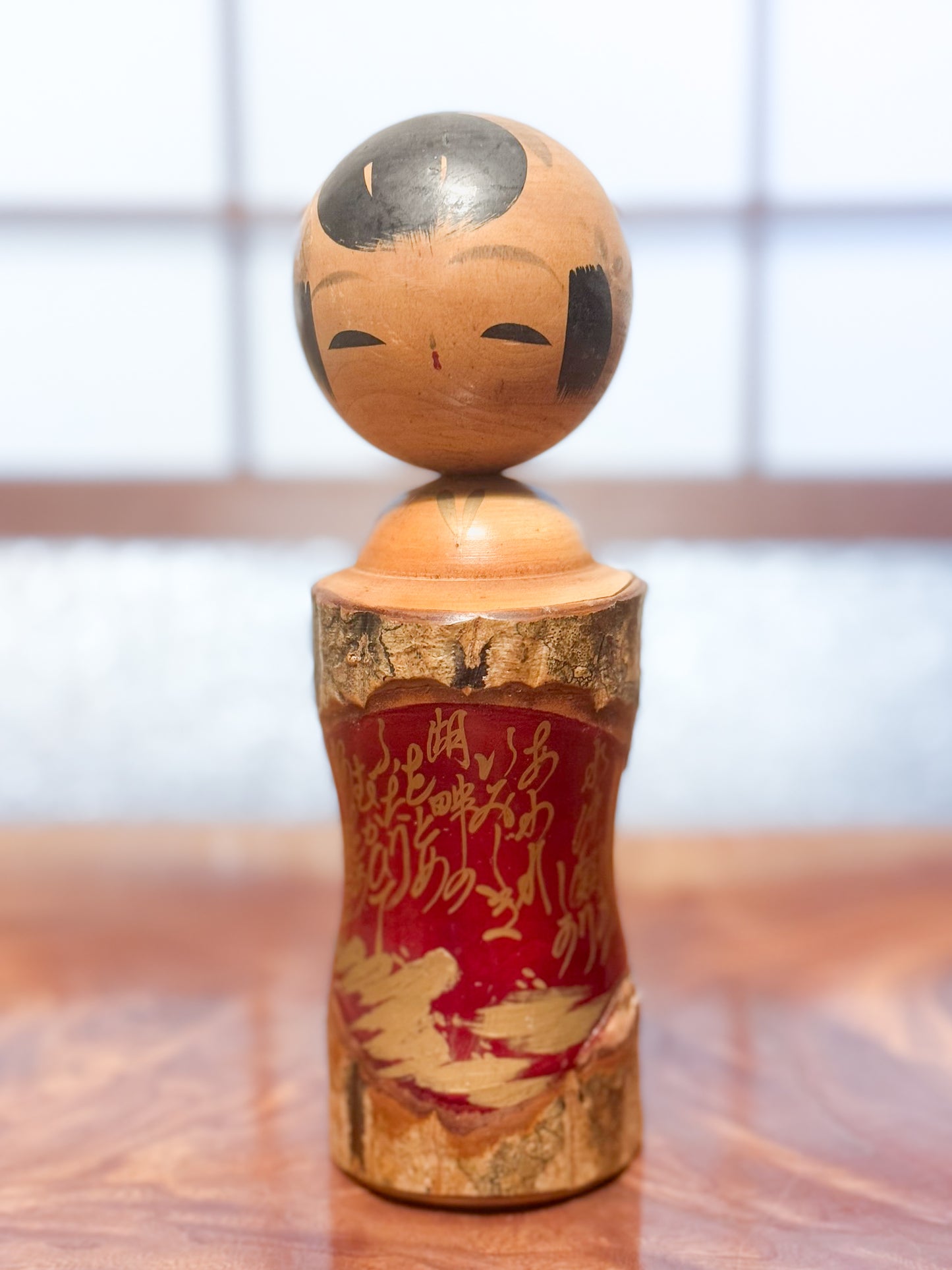Kokeshi en bois brut avec écorce et laque rouge, décorée de kanji dorés