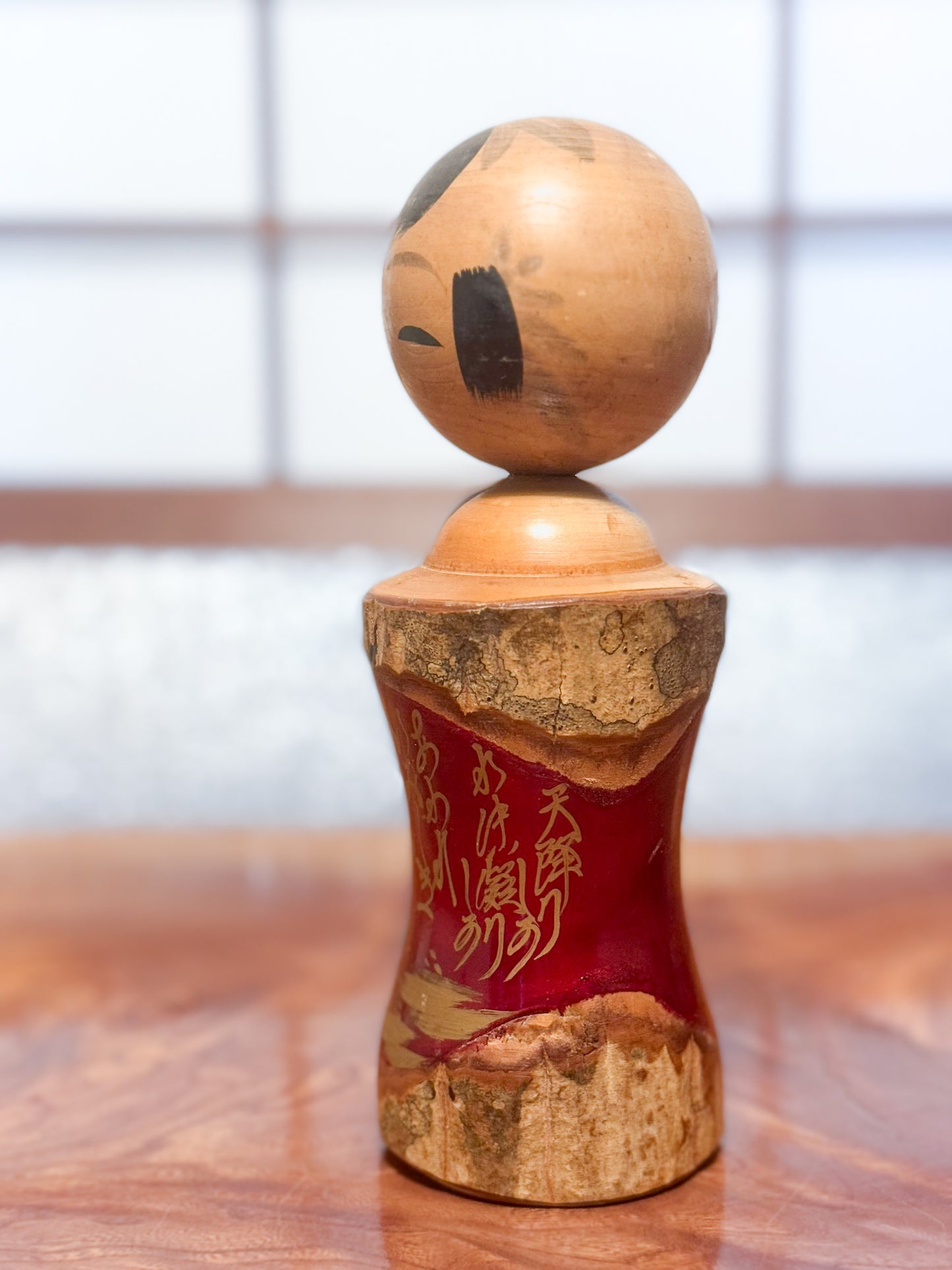 Kokeshi en bois brut avec écorce et laque rouge, décorée de kanji dorés, profil gauche