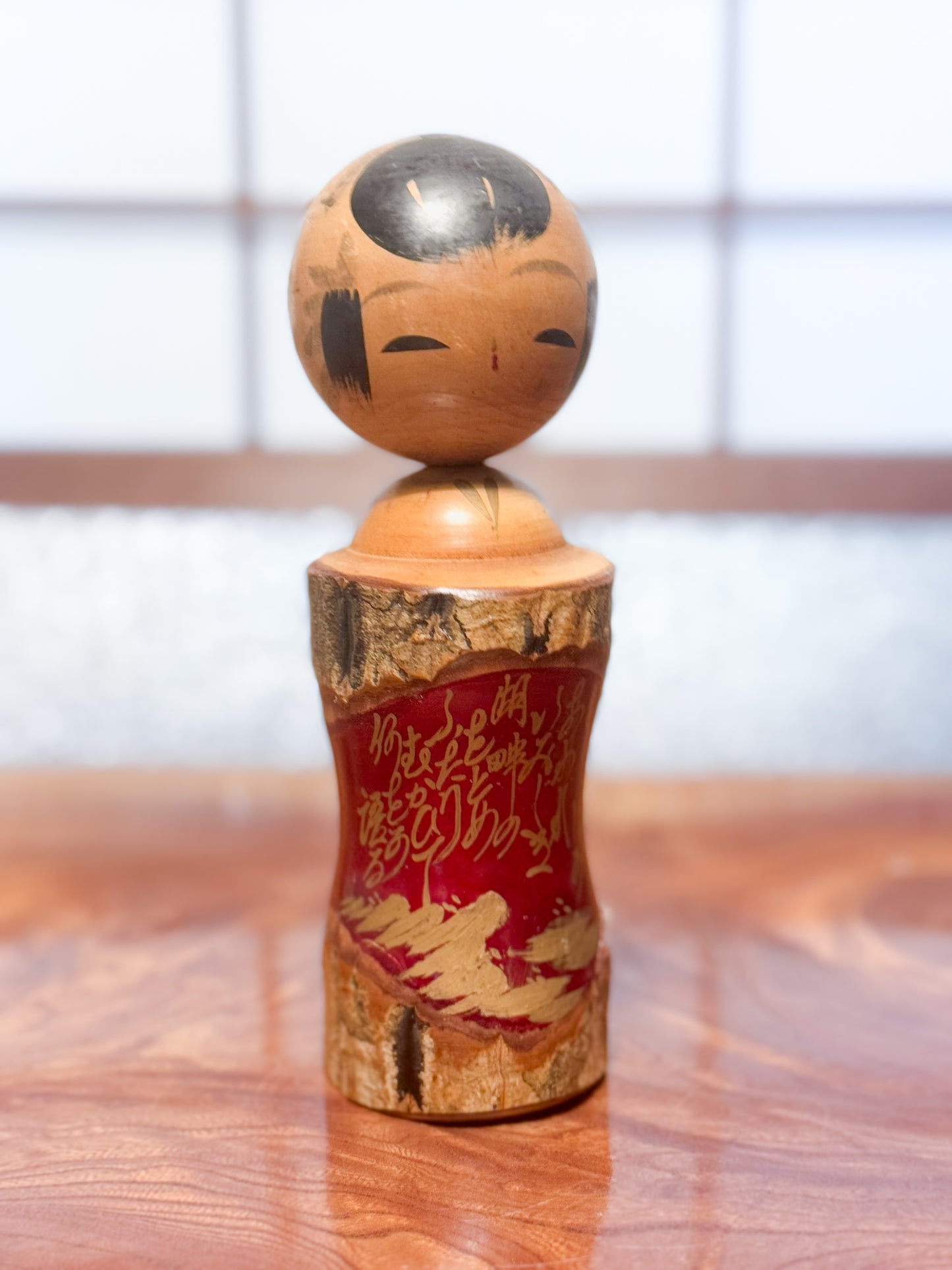 Kokeshi en bois brut avec écorce et laque rouge, décorée de kanji dorés, vu de 3/4 droite