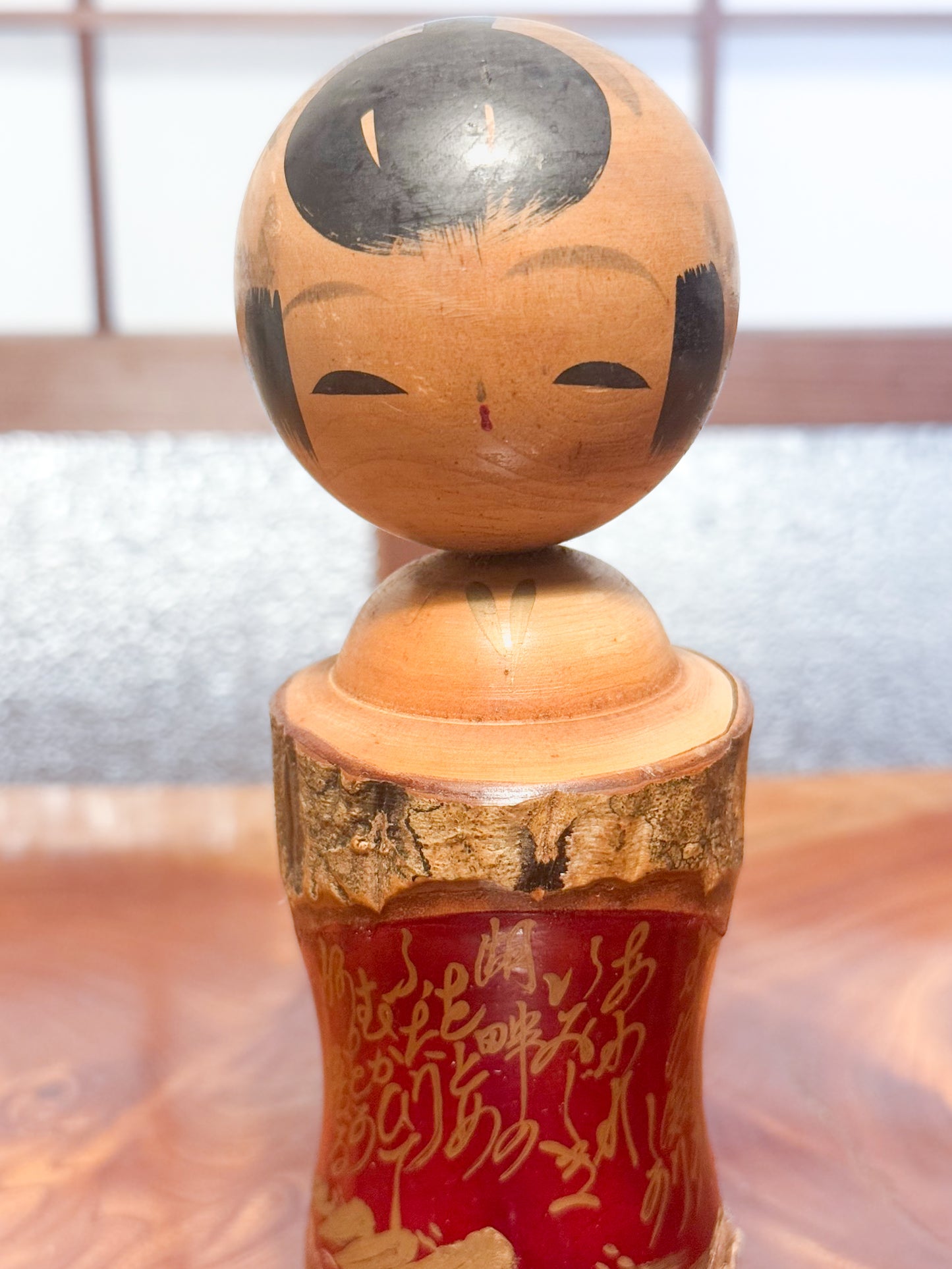 Kokeshi en bois brut avec écorce et laque rouge, décorée de kanji dorés, gros plan sur la tête