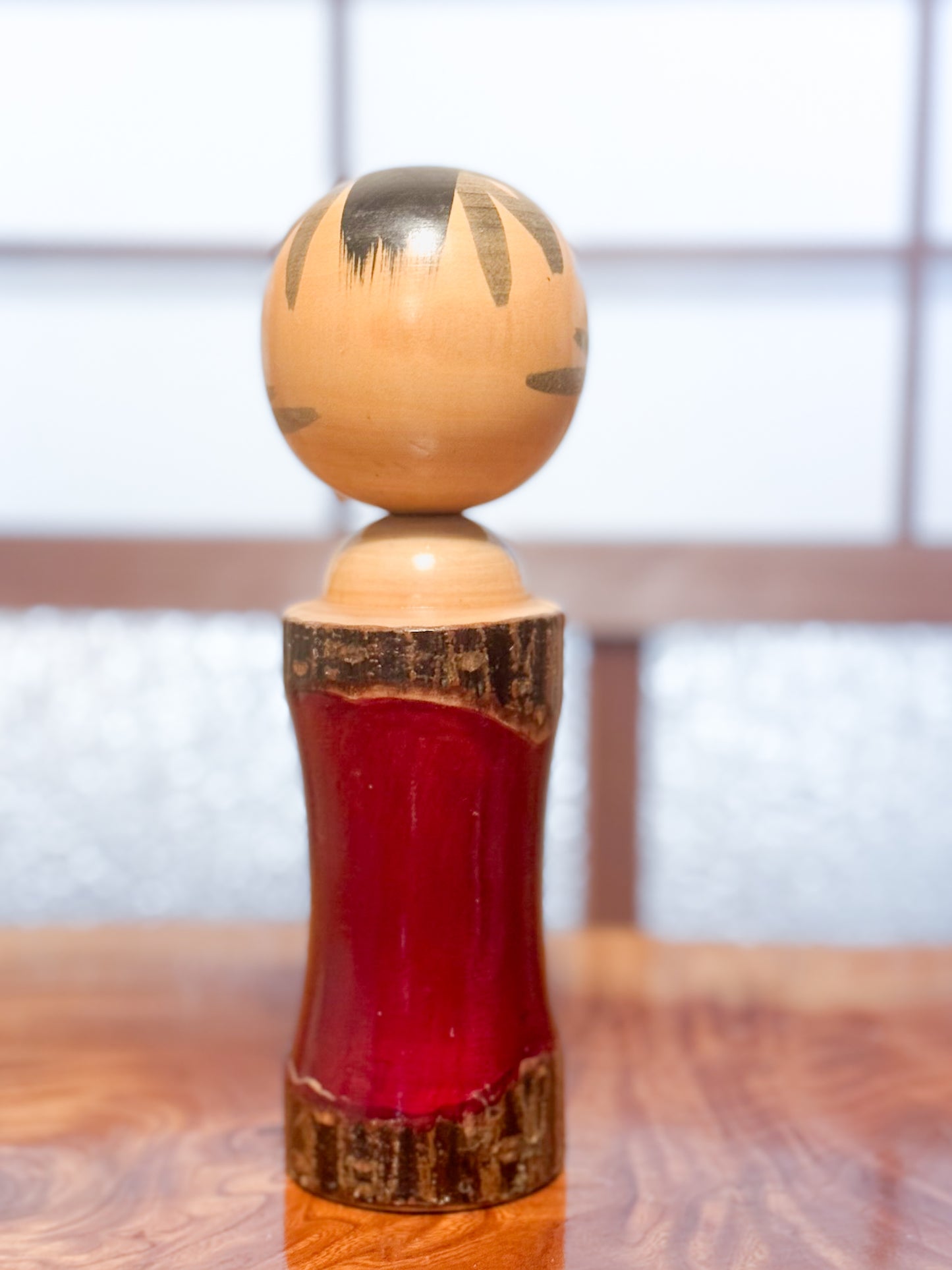 Kokeshi en bois brut avec laque rouge et kanji "zen" doré, vu de dos