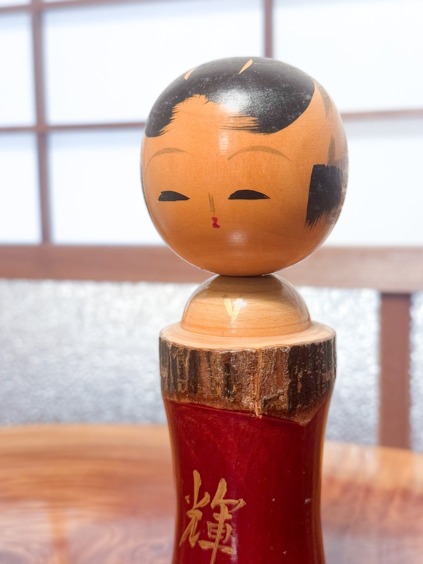Kokeshi en bois brut avec laque rouge et kanji "zen" doré, gros plan sur le visage