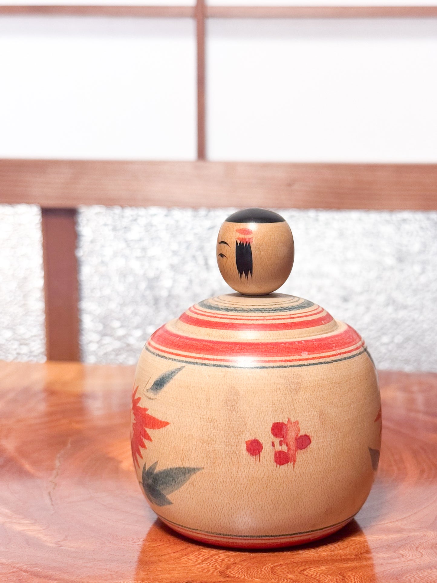 Kokeshi ronde évoquant un bébé dans son panier, décorée de grands chrysanthèmes rouges sur bois clair, profil gauche