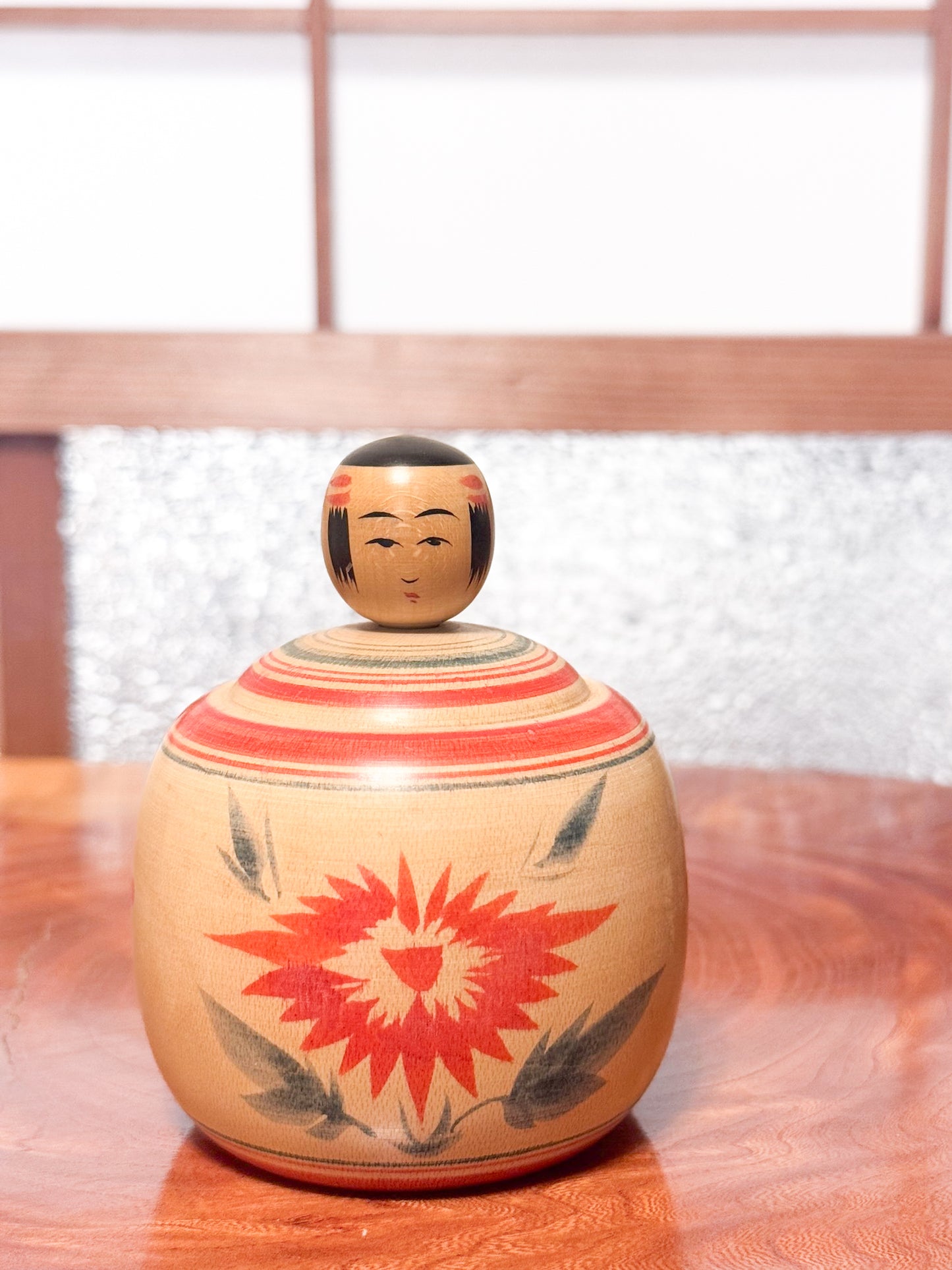 Kokeshi ronde évoquant un bébé dans son panier, décorée de grands chrysanthèmes rouges sur bois clair, face