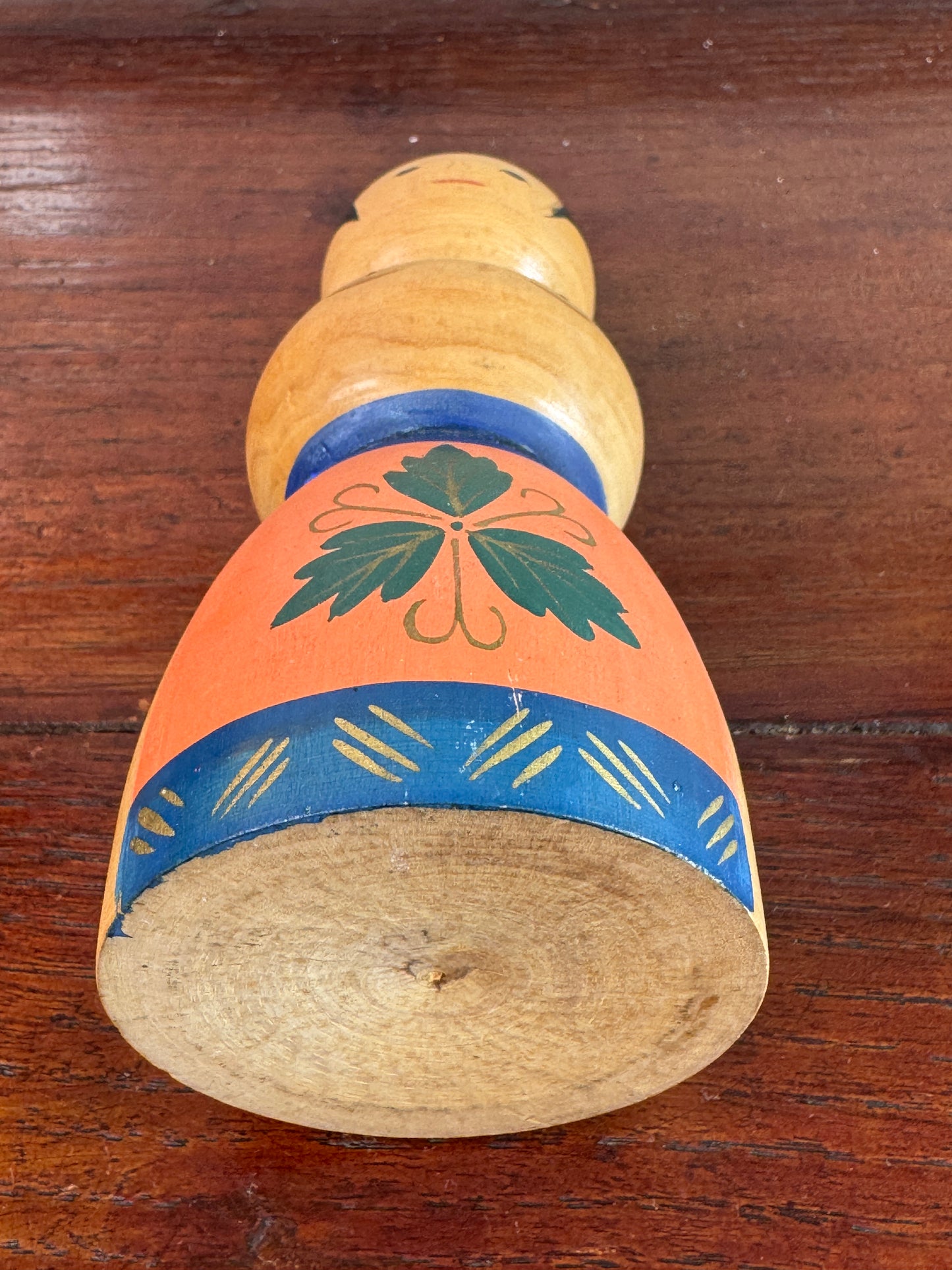 Kokeshi japonaise vintage représentant un sumo, en bois peint avec tablier au motif végétal stylisé, dessous
