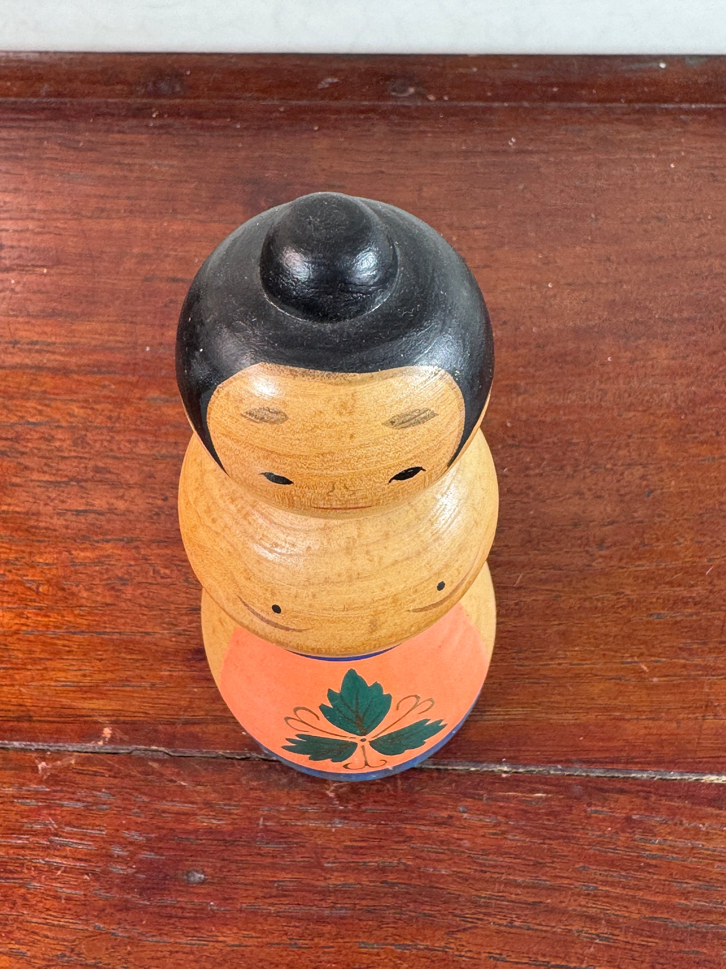Kokeshi japonaise vintage représentant un sumo, en bois peint avec tablier au motif végétal stylisé, vu de dessus