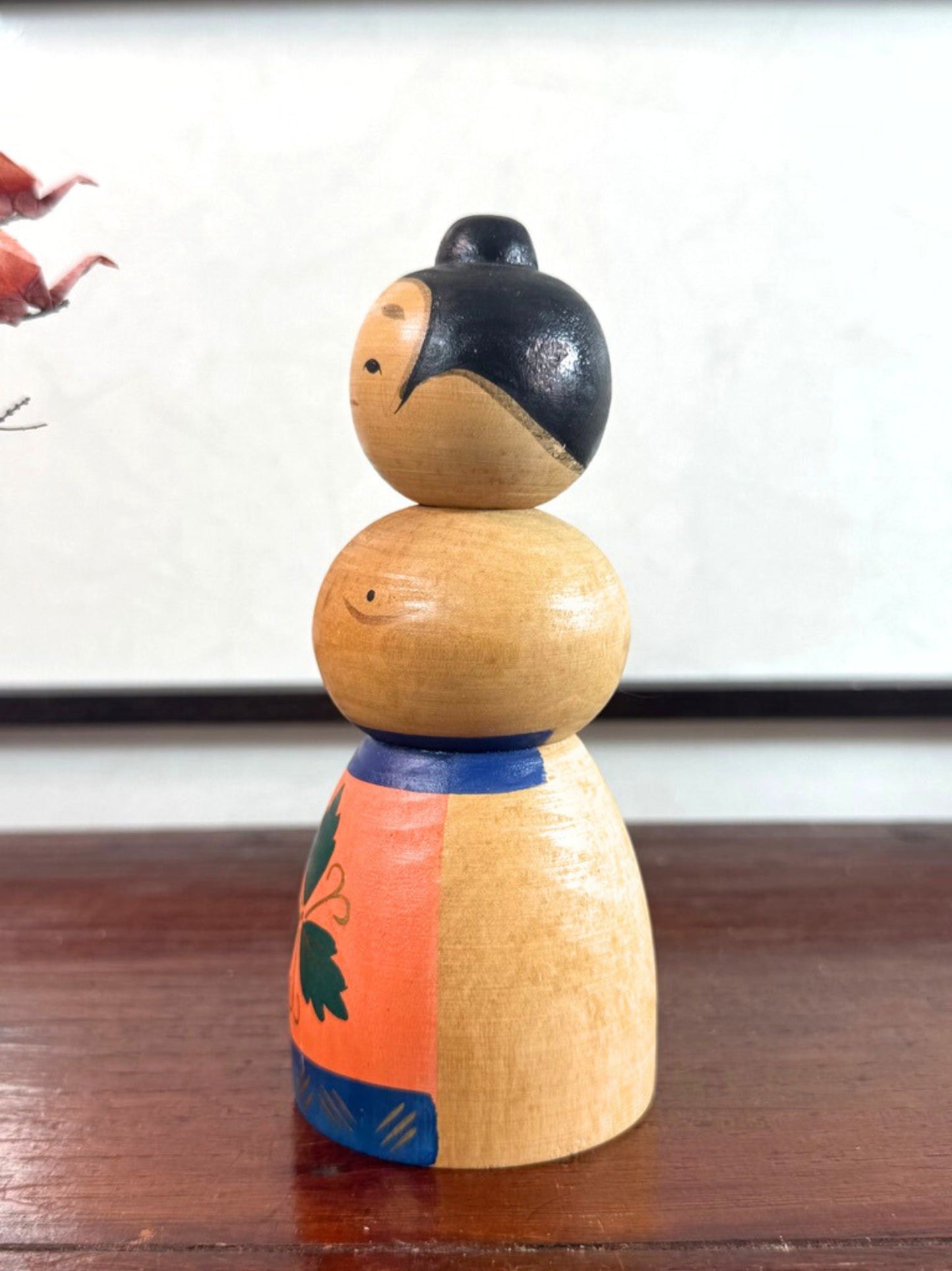 Kokeshi japonaise vintage représentant un sumo, en bois peint avec tablier au motif végétal stylisé, vu du profil gauche