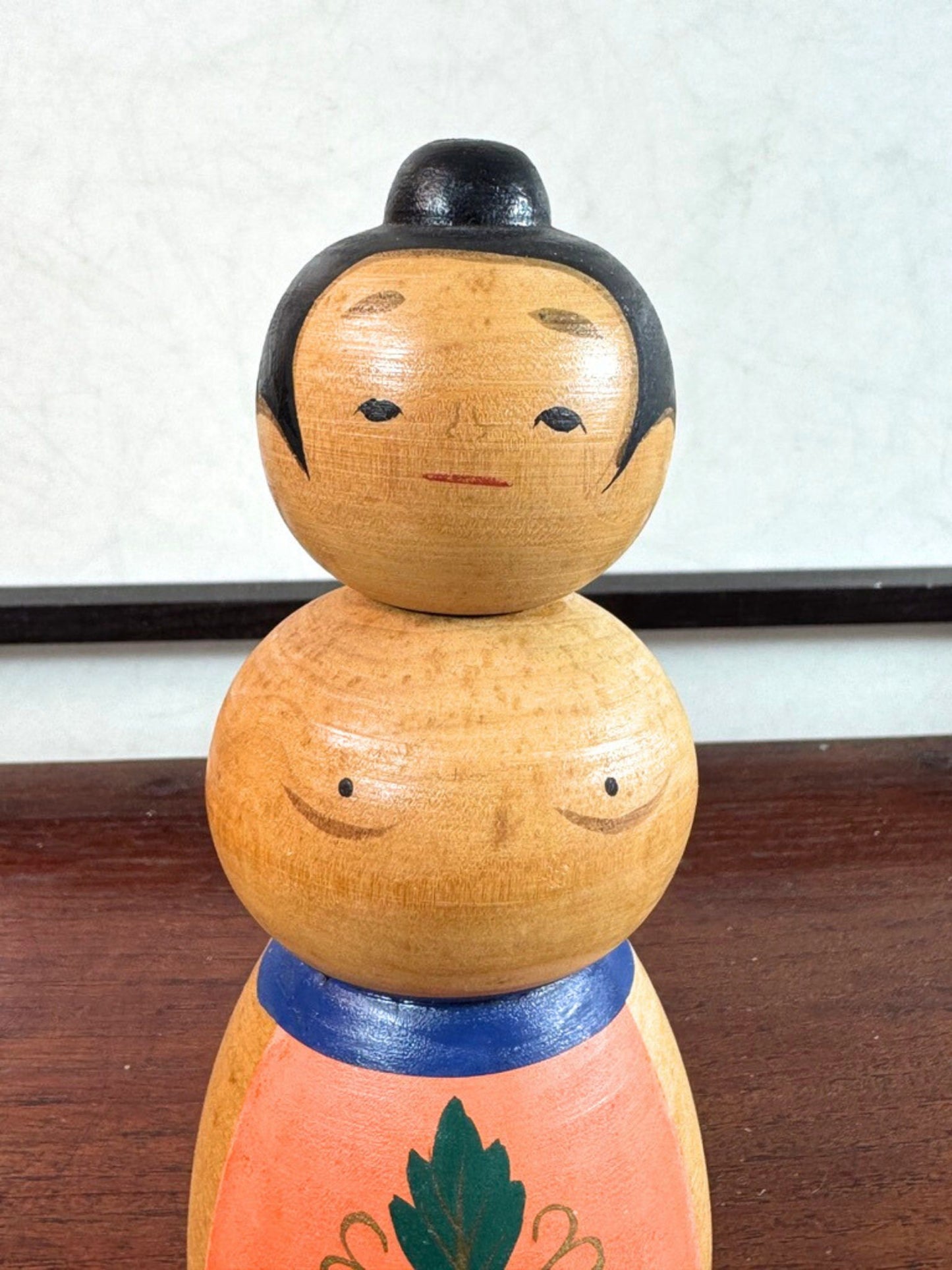 Kokeshi japonaise vintage représentant un sumo, en bois peint avec tablier au motif végétal stylisé, gros plan sur le buste