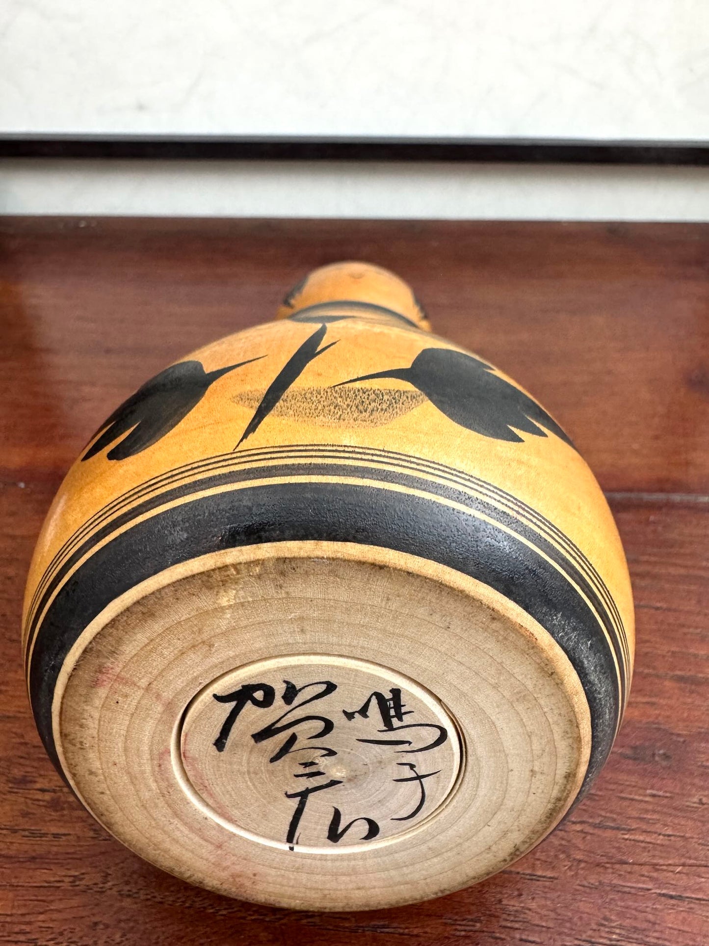 Poupée Japonaise Kokeshi nemariko de Sato Yoshihiro, avec un grand chrysanthème noir peint à la main, vu de dessous la signature de l'artisan