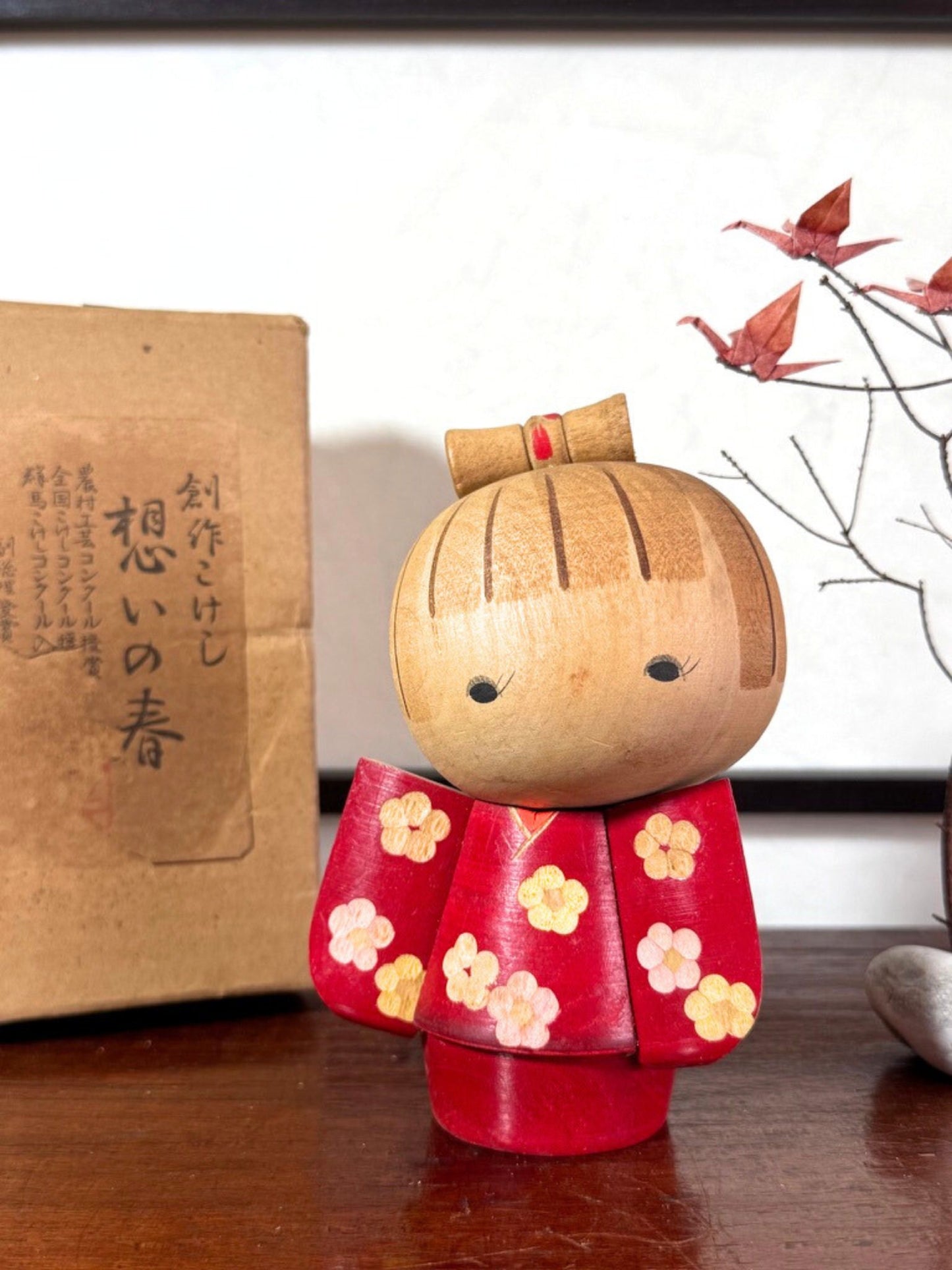 Kokeshi japonaise rouge avec fleurs, coiffée d’un nœud, signée Kazuo Takamizawa; avec boite d'origine