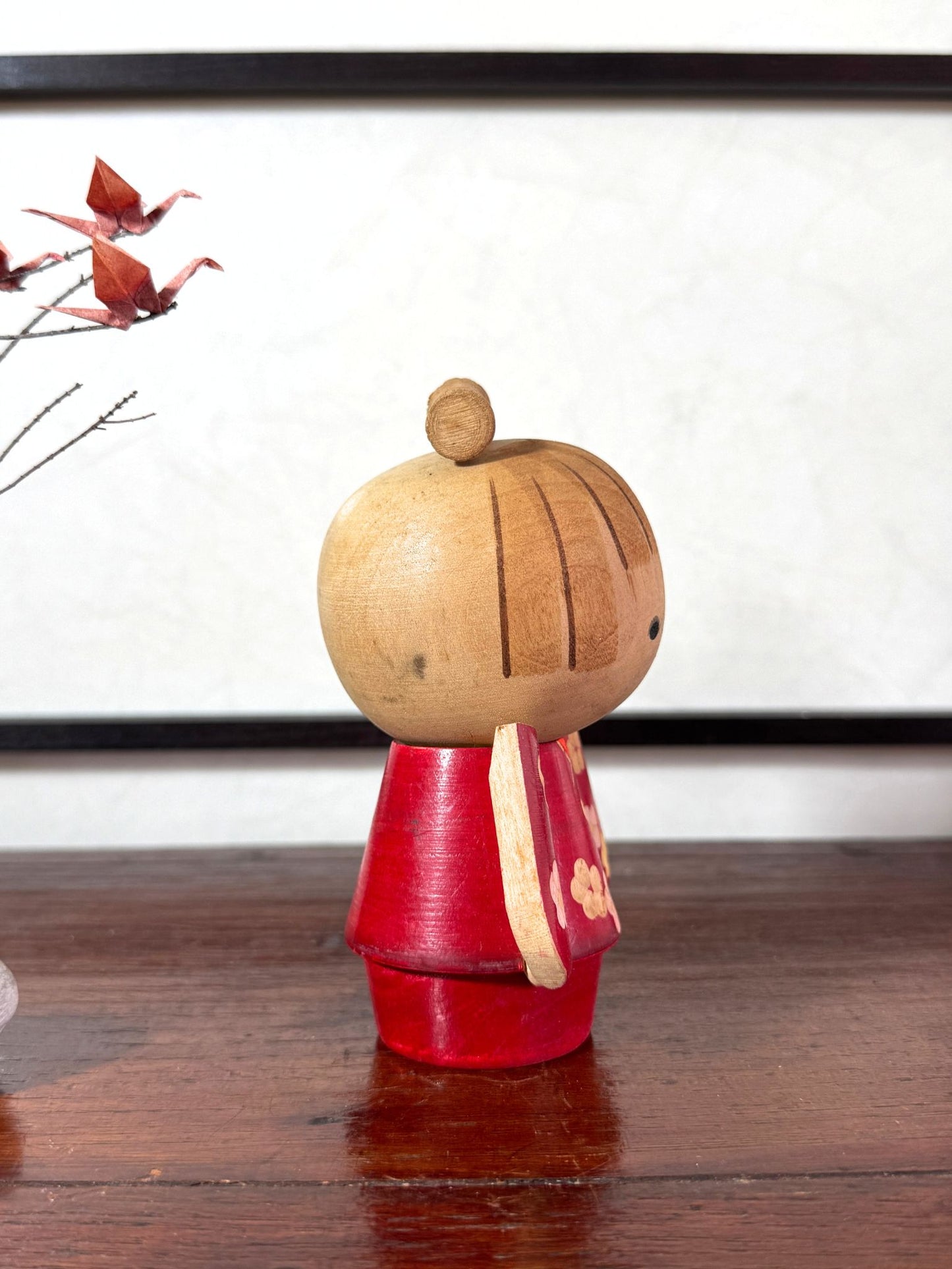 Kokeshi japonaise rouge avec fleurs, coiffée d’un nœud, signée Kazuo Takamizawa, profil droit
