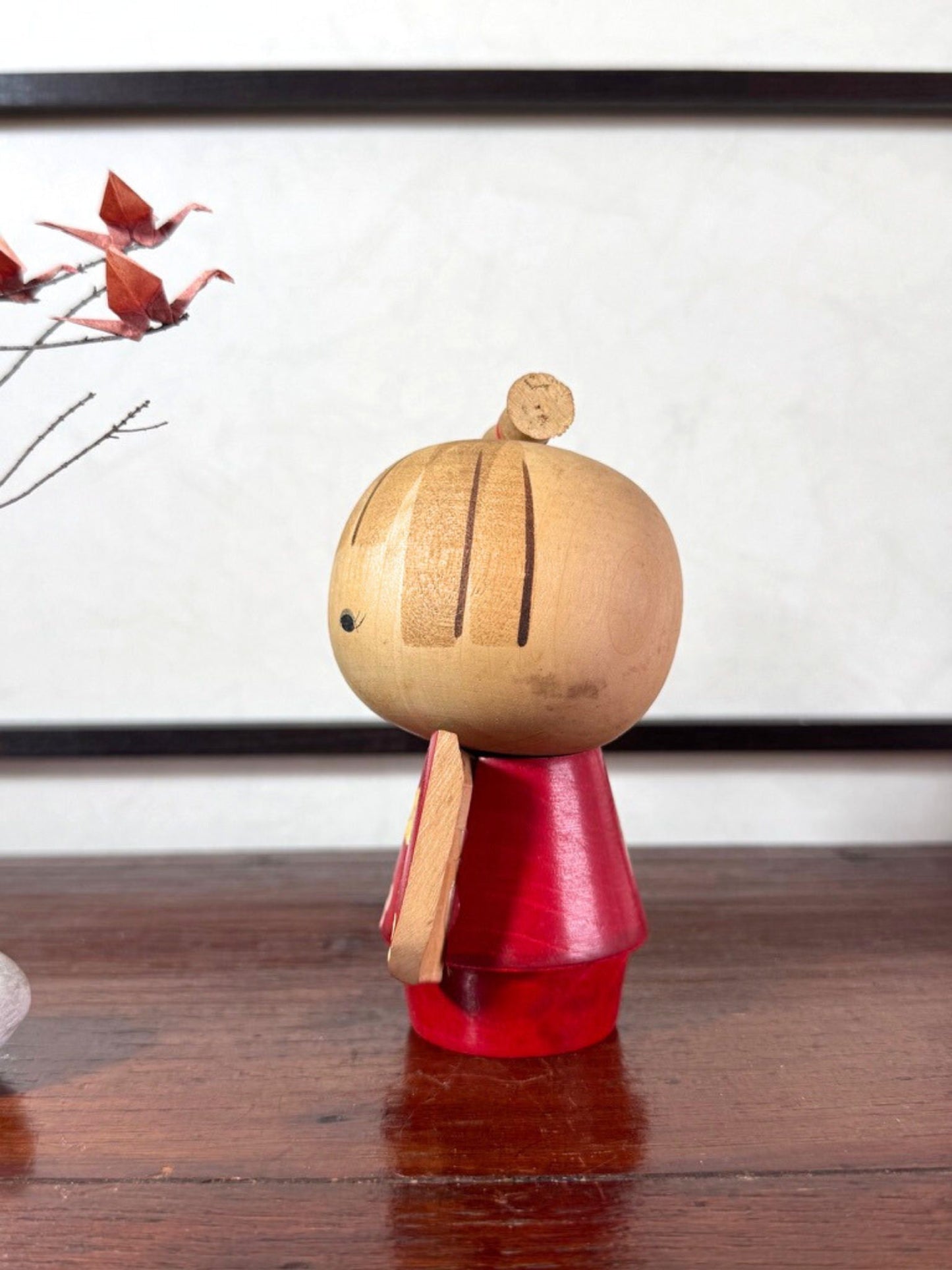 Kokeshi japonaise rouge avec fleurs, coiffée d’un nœud, signée Kazuo Takamizawa, profil gauche