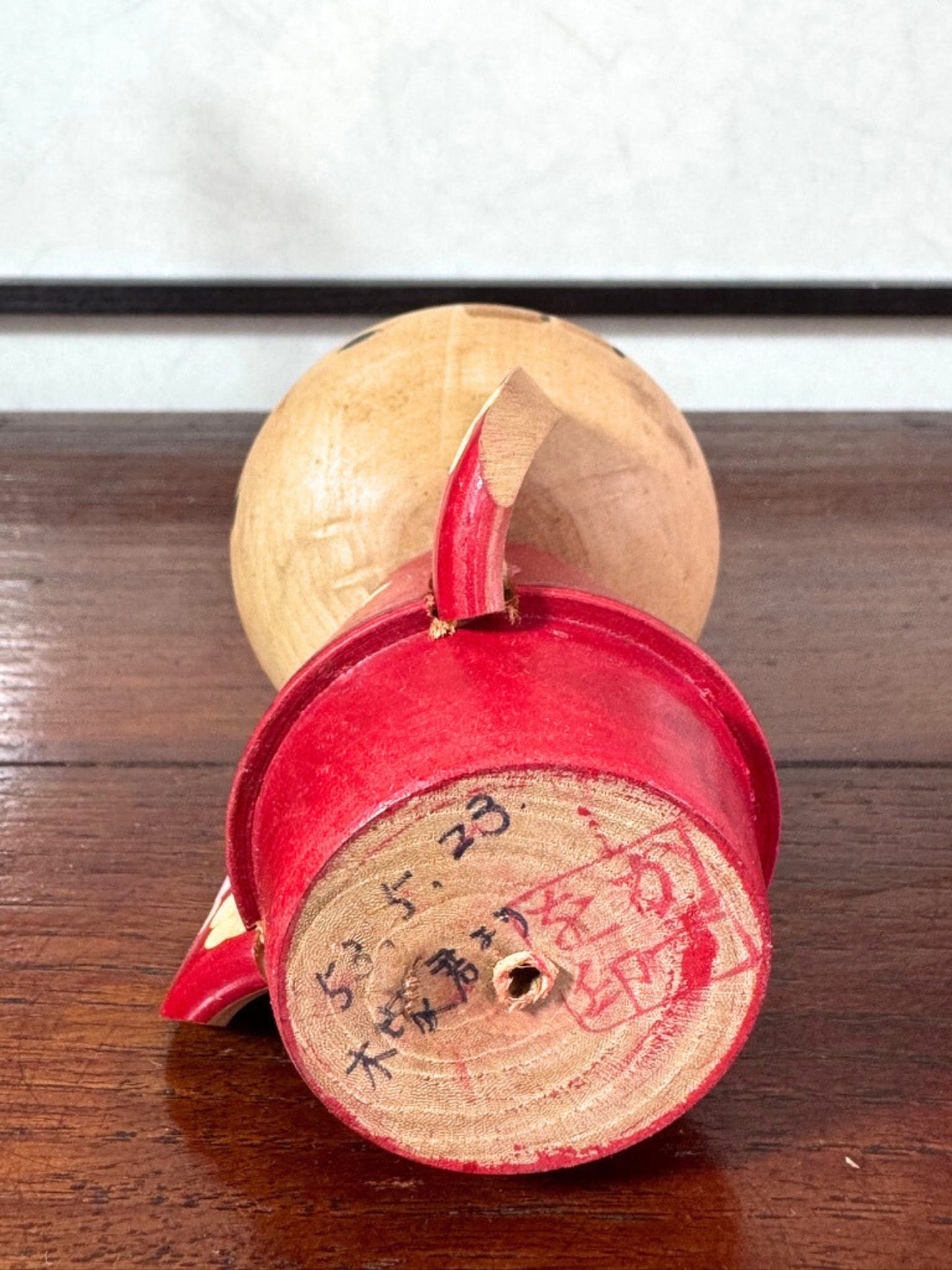 Kokeshi japonaise rouge avec fleurs, coiffée d’un nœud, signée Kazuo Takamizawa, le dessous avec le sceau de l'artisan