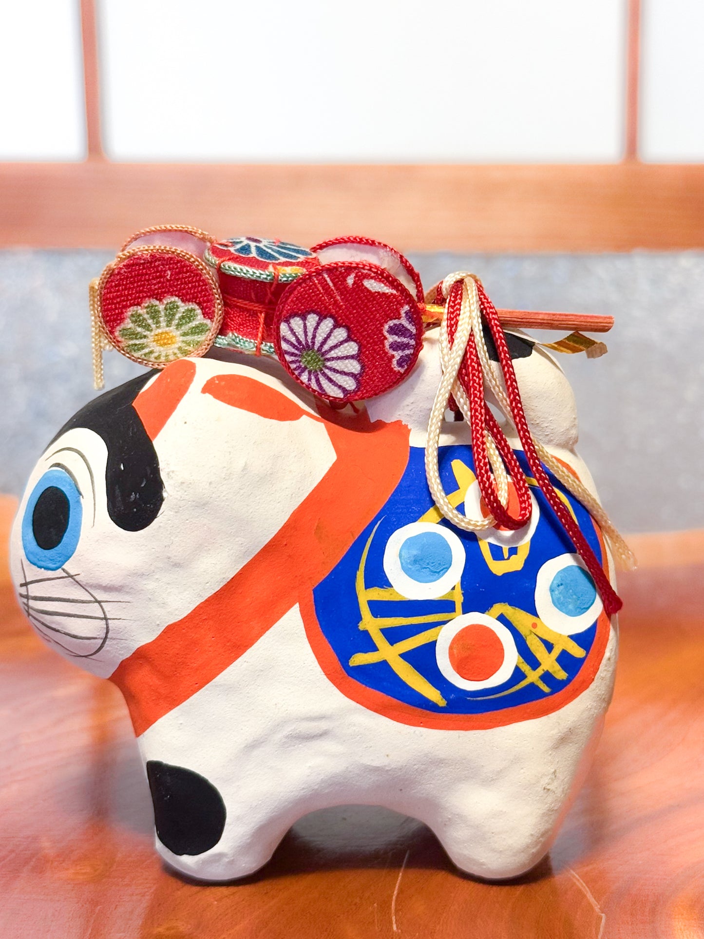 Figurine japonaise en papier mâché représentant un inu hariko blanc décoré, avec panier en bambou et tambours miniatures sur le dos, motif peint profil gauche