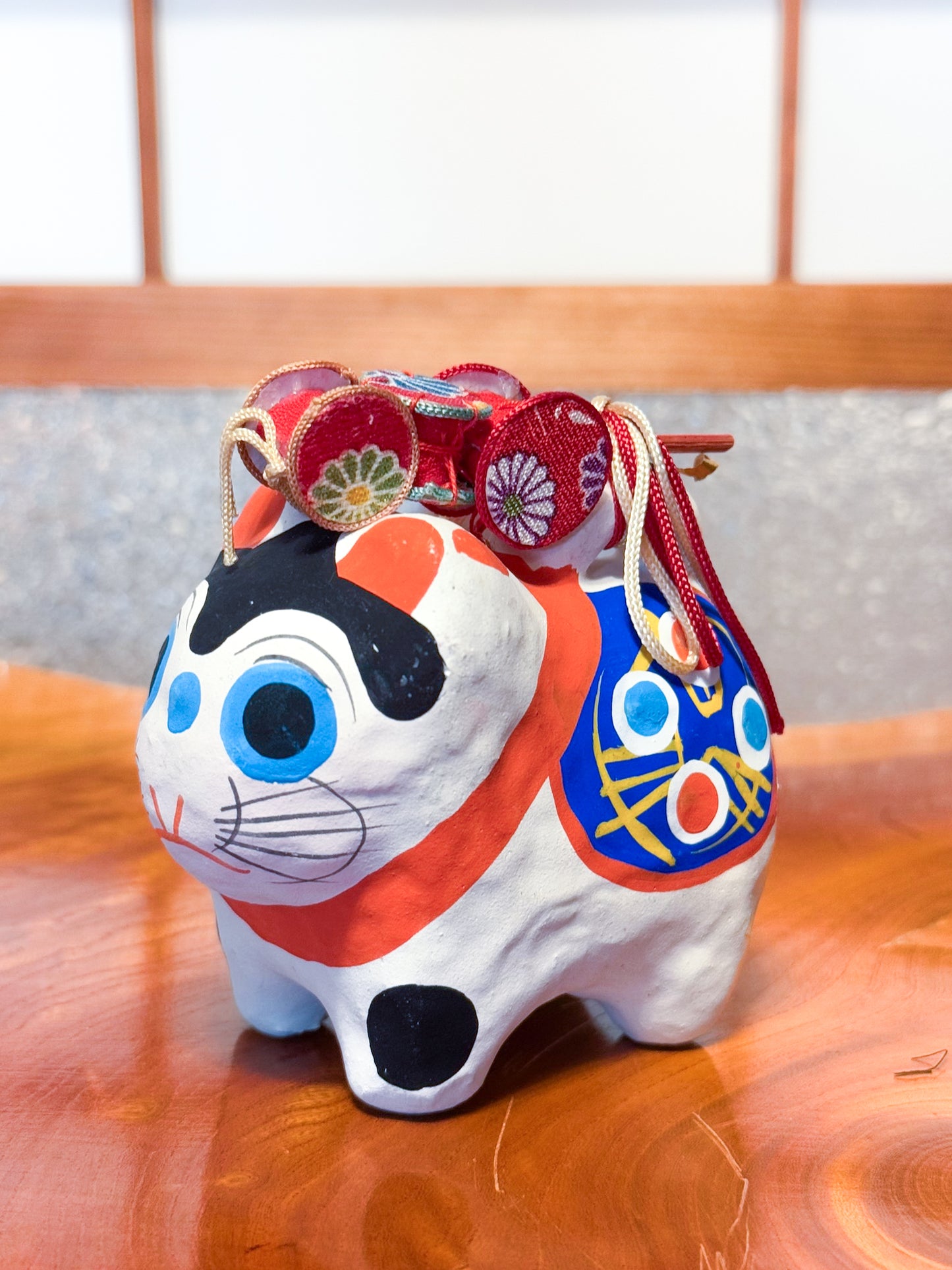 Figurine japonaise en papier mâché représentant un inu hariko blanc décoré, avec panier en bambou et tambours miniatures sur le dos, vu de 3/4