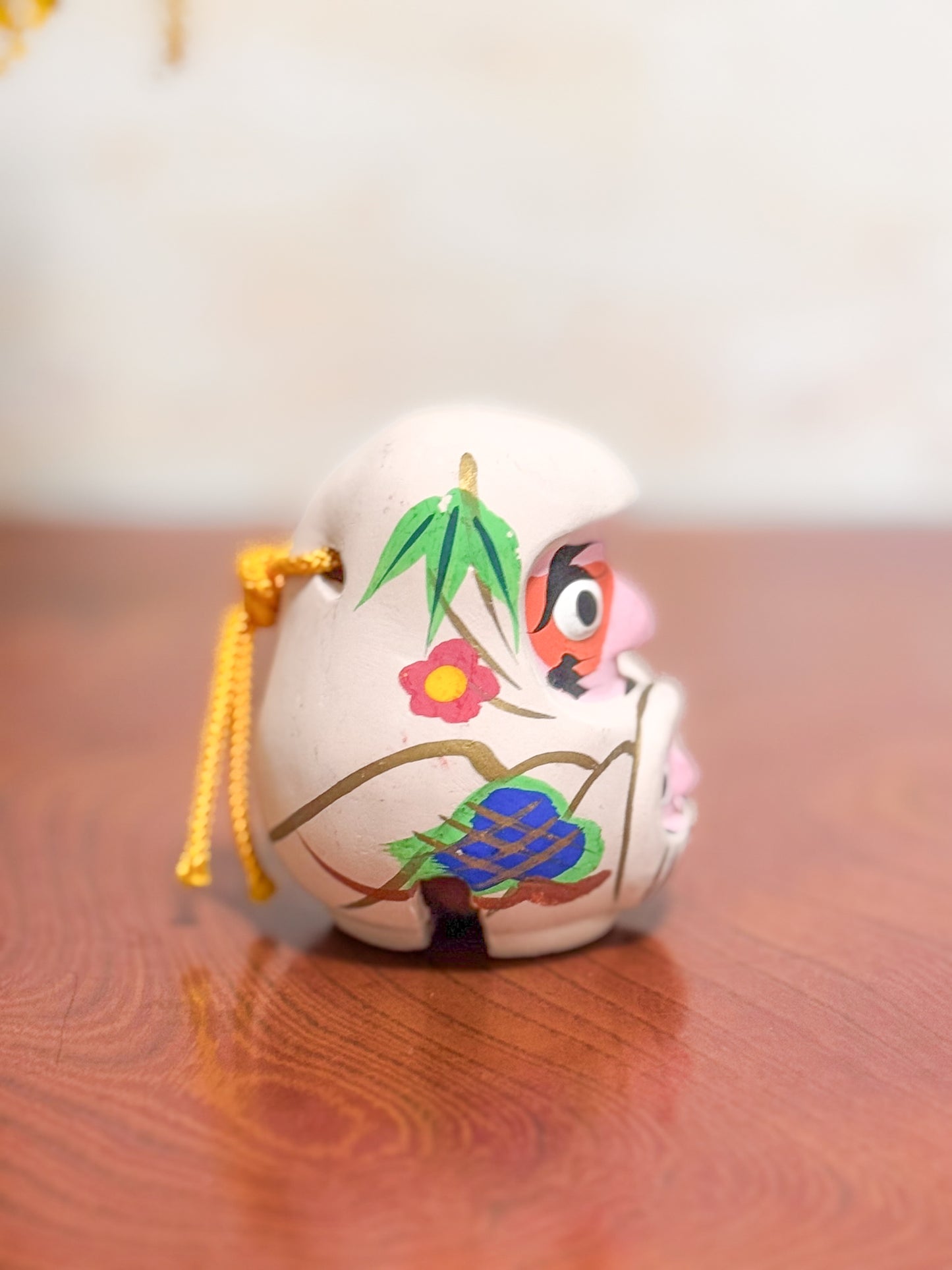 Clochette japonaise en terre cuite peinte à la main représentant deux daruma, adulte et enfant, ornée de fleurs et motifs traditionnels, profil droit