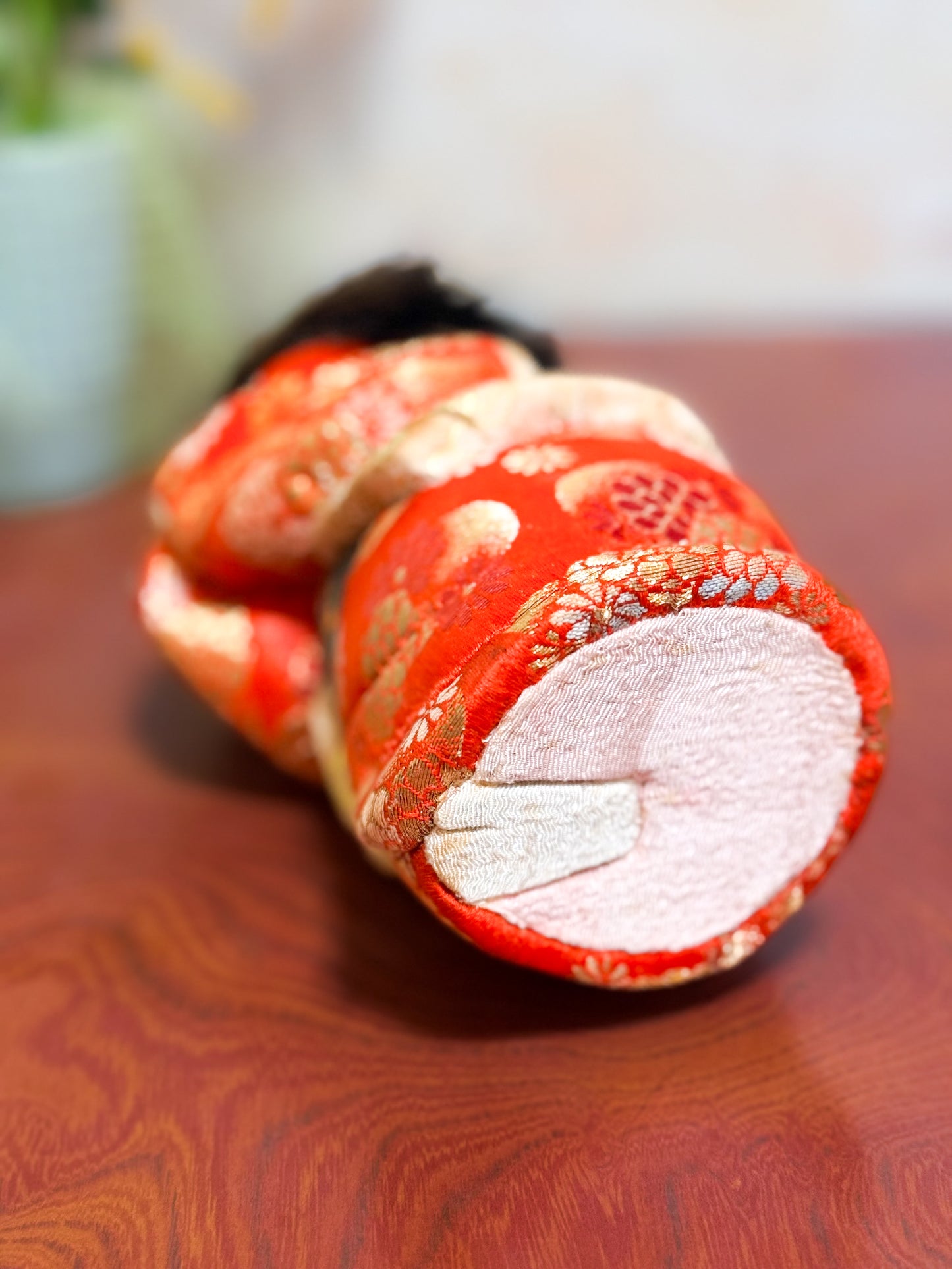 Poupée japonaise kimekomi représentant une jeune fille en kimono rouge fleuri avec les mains jointes, coiffée d’un chignon traditionnel, vu de dessous