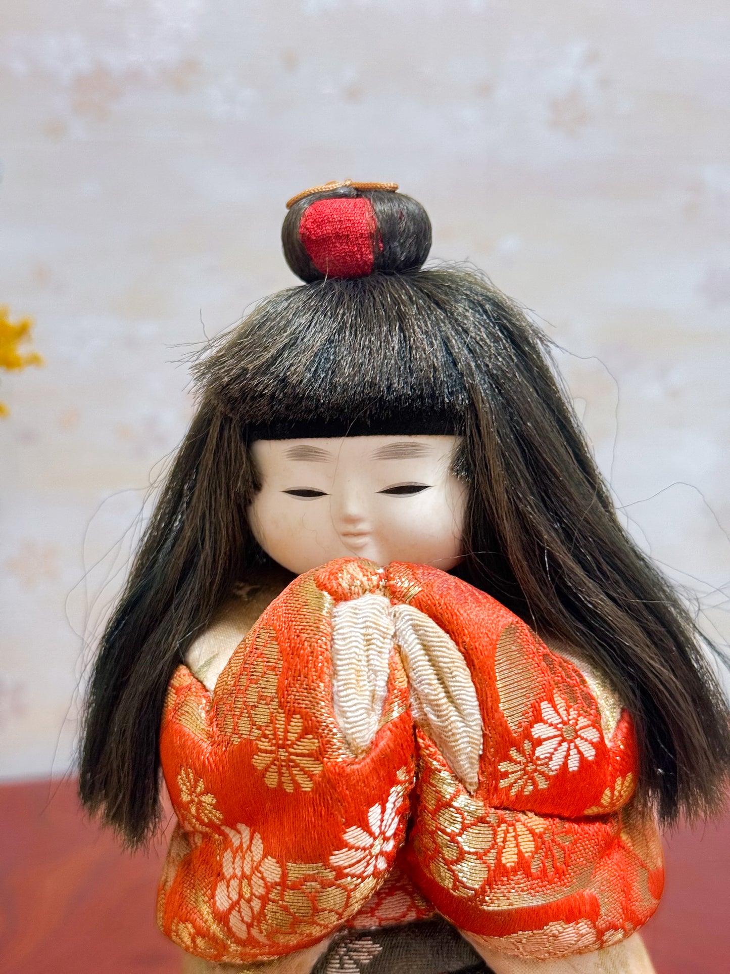 Poupée japonaise kimekomi représentant une jeune fille en kimono rouge fleuri avec les mains jointes, coiffée d’un chignon traditionnel, gros plan sur le visage