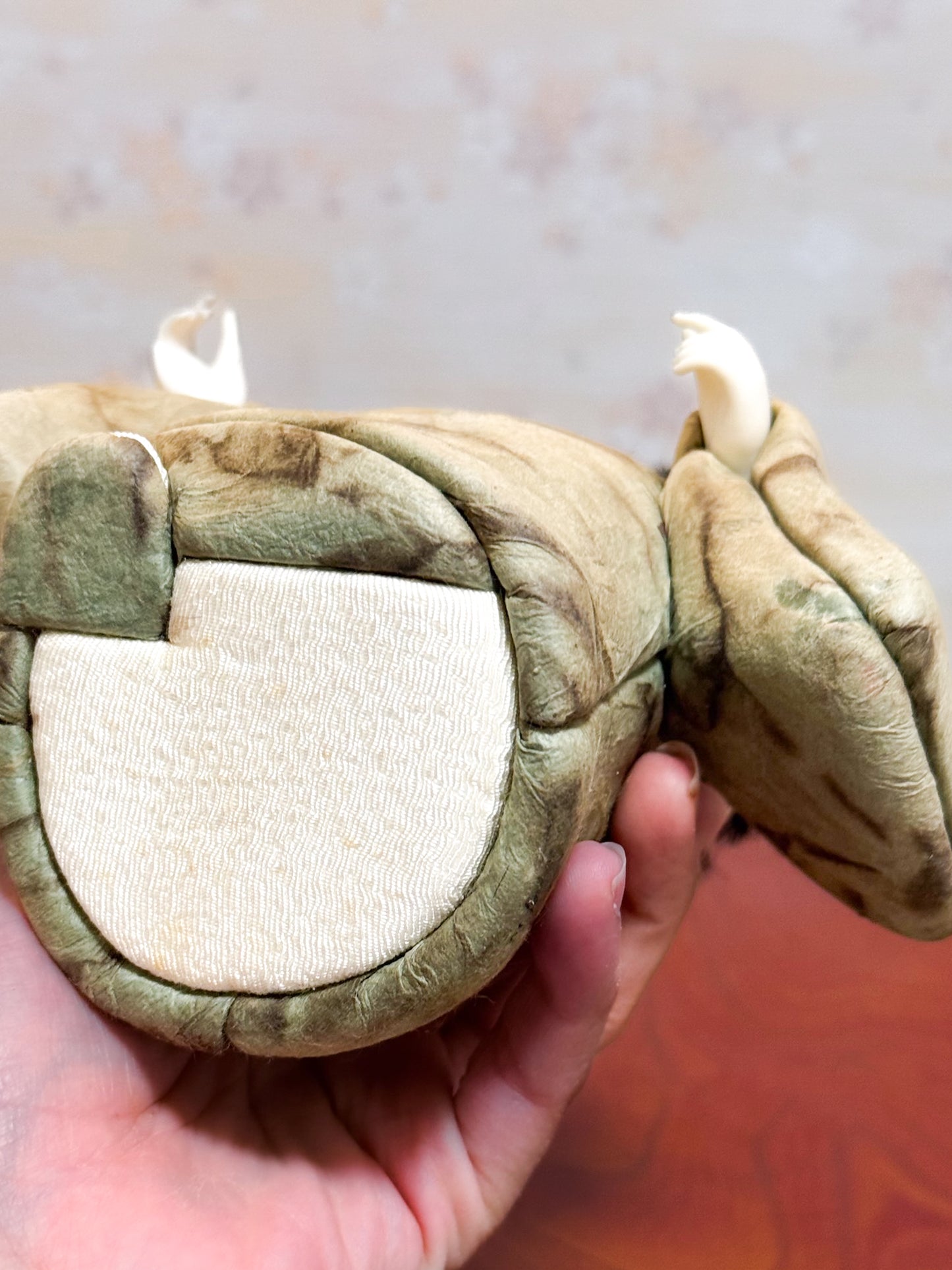 Poupée japonaise kimekomi représentant un enfant en kimono beige tenant une boîte à tabac rouge, vu de dessous