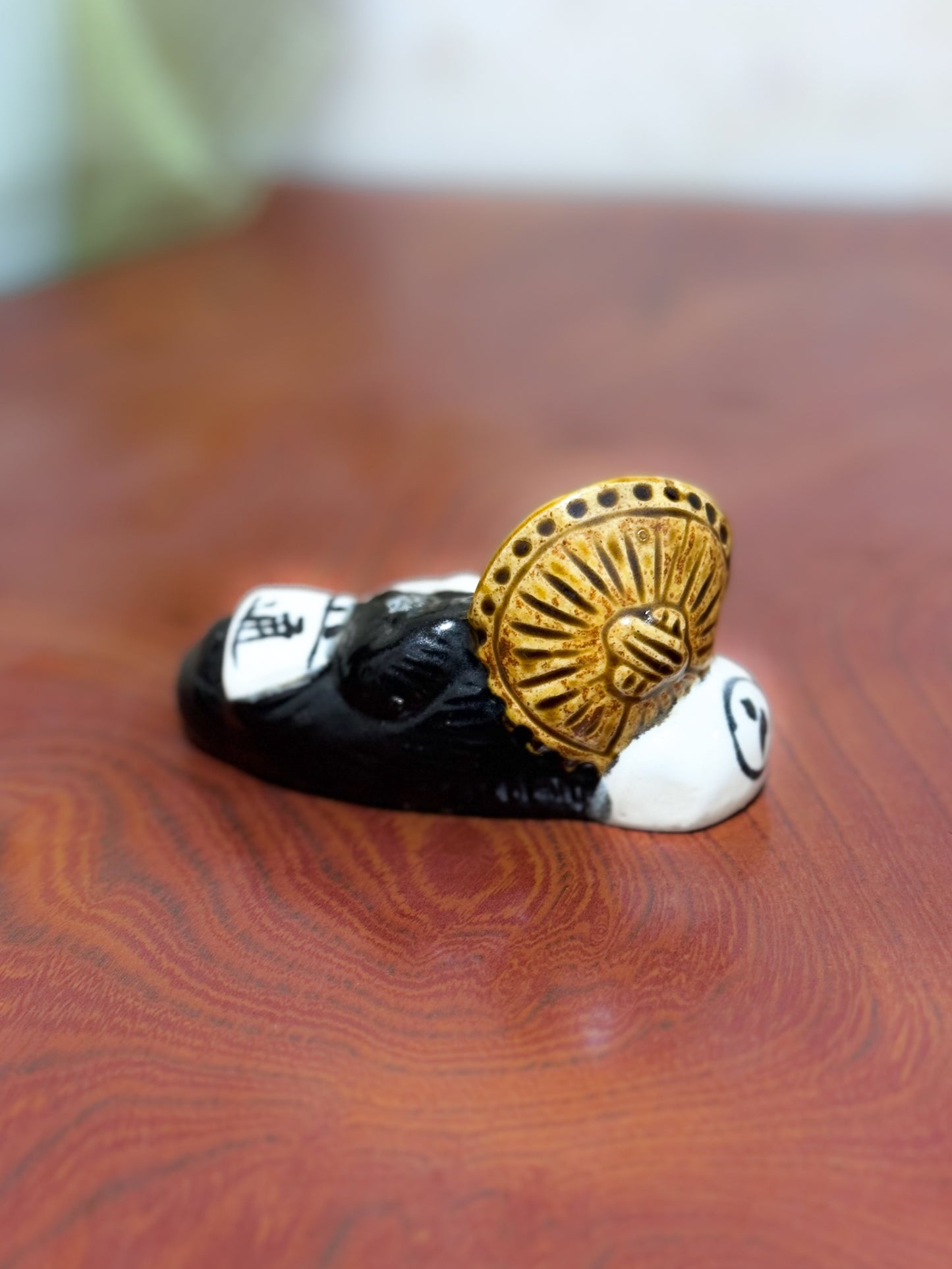 Figurine en céramique d’un tanuki allongé sur une bouteille de saké portant le kanji 福, symbole de bonheur et de prospérité au Japon, vu de dos