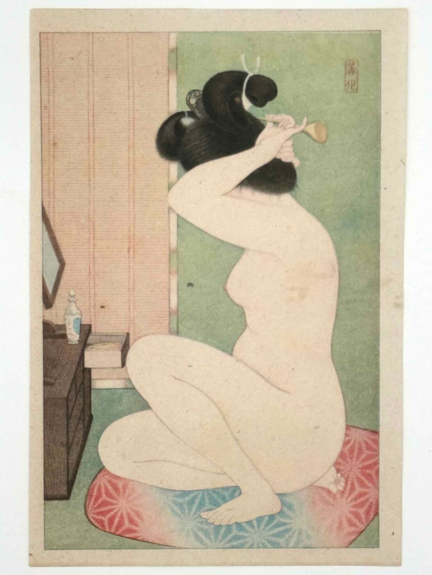 Lithographie Japonaise portrait de femme nue après le bain, assise de profil sur coussin rouge et bleu, en train de mettre une épingle dans ses cheveux face à un miroir.