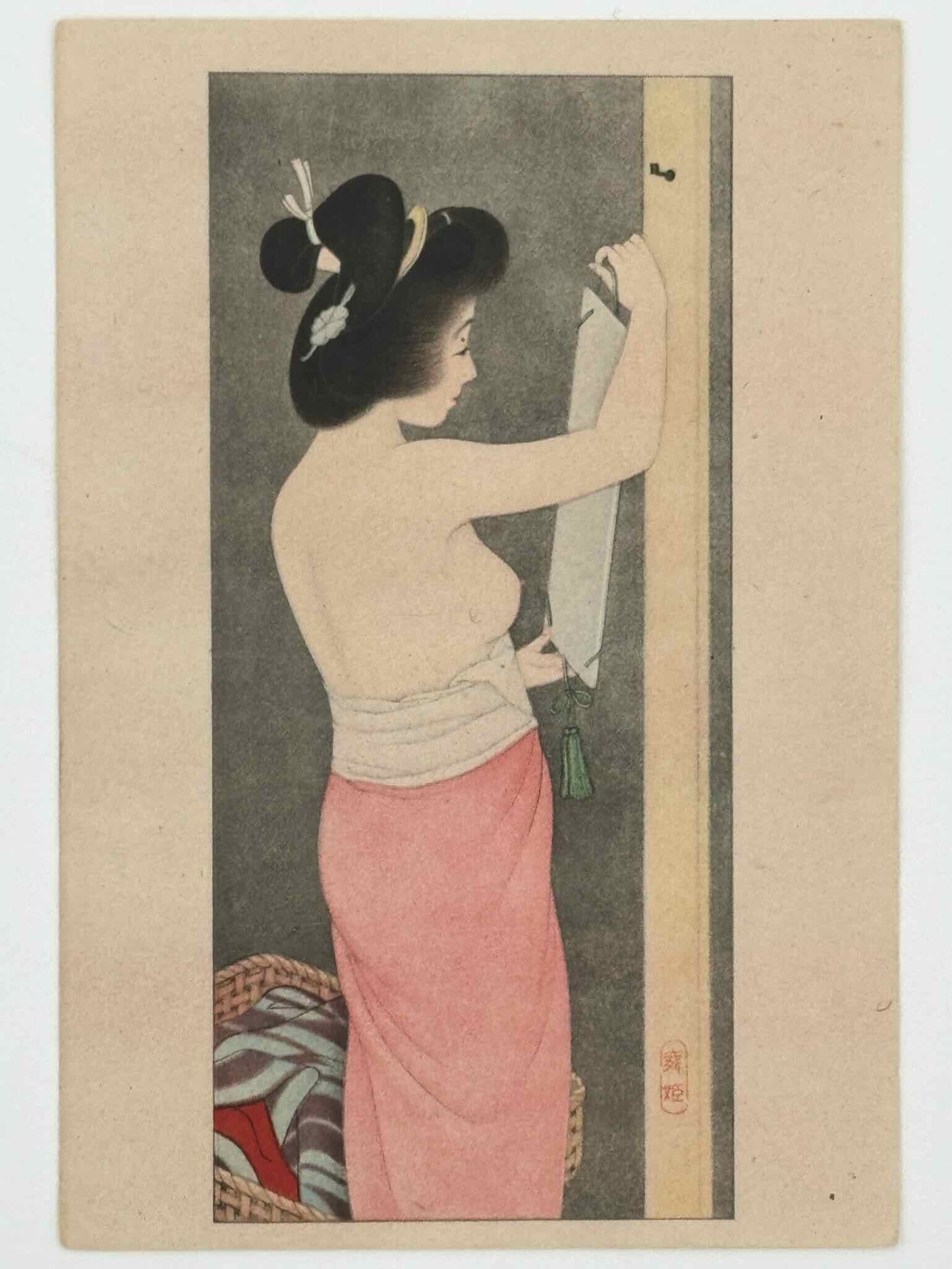 Lithographie Japonaise d'une femme à demi-nue accrochant un miroir au mur. Elle porte un bas de couleur rose, poitrine nue