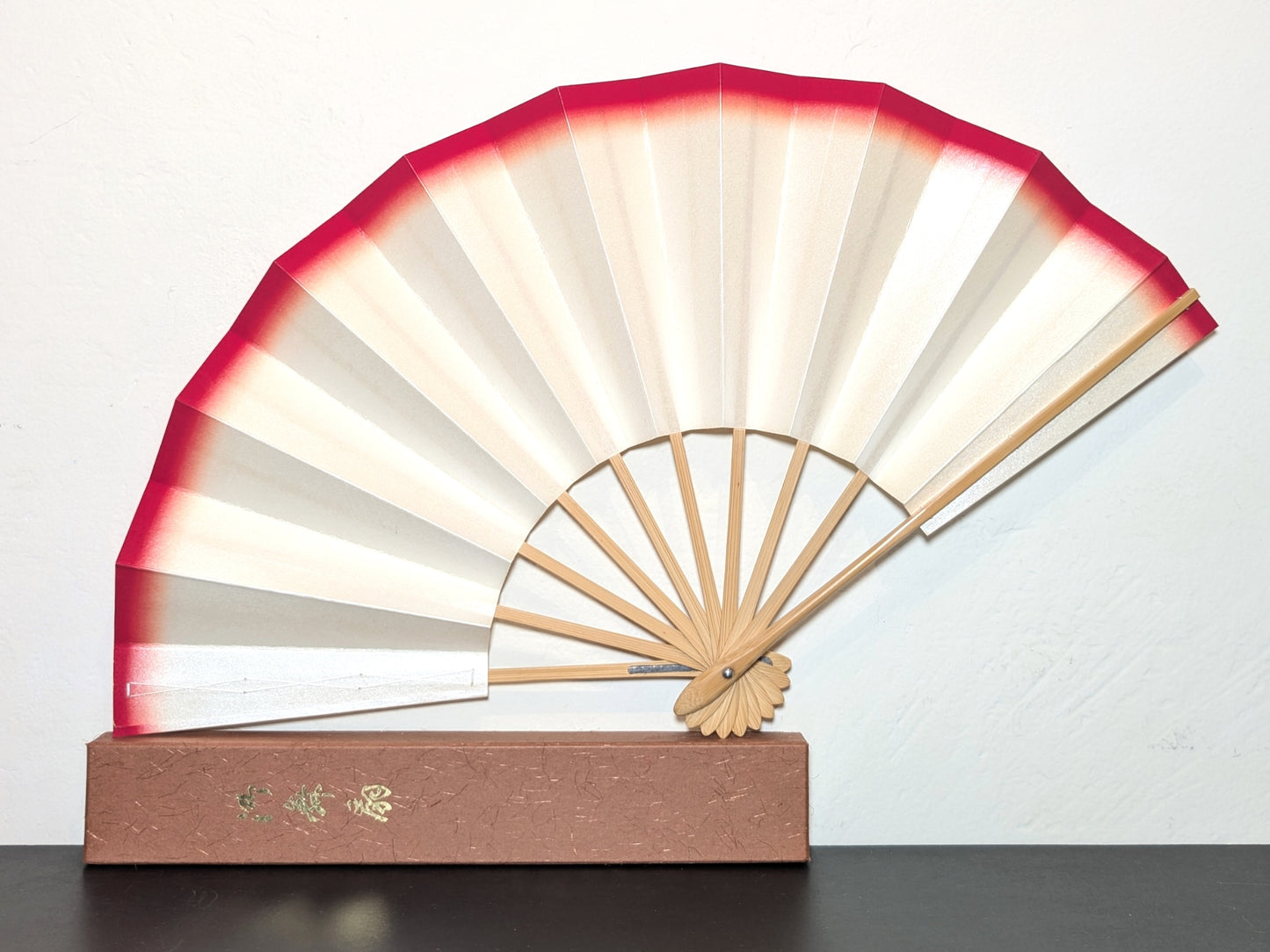 Eventail traditionnel japonais de théâtre kabuki monté sur bambou. Couleur blanc micacé et rebord rouge. Présenté sur sa boite cartonnée couleur sienne. Avec calligraphie dorée sur le couvercle.