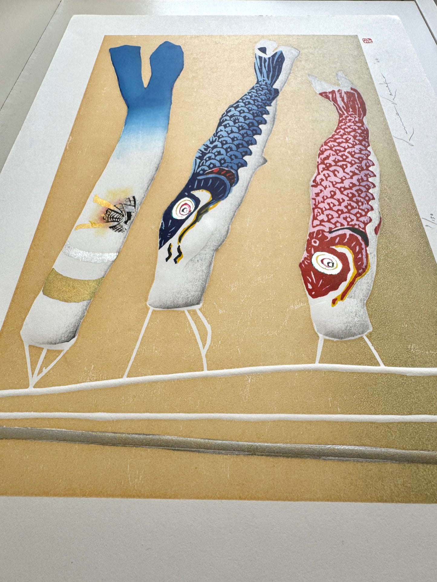 Estampe japonaise avec trois koinobori colorés et un casque kabuto sur fond doré par Kunio Kaneko, vue de profil détail du gaufrage et reflets dorés et argentés
