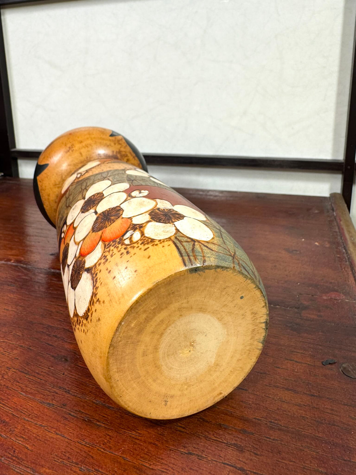 Kokeshi vintage de Yuji Kawase datée de 1985, au petit chignon et kimono orné de fleurs blanches gravées évoquant le cerisier ou le prunier, le dessous