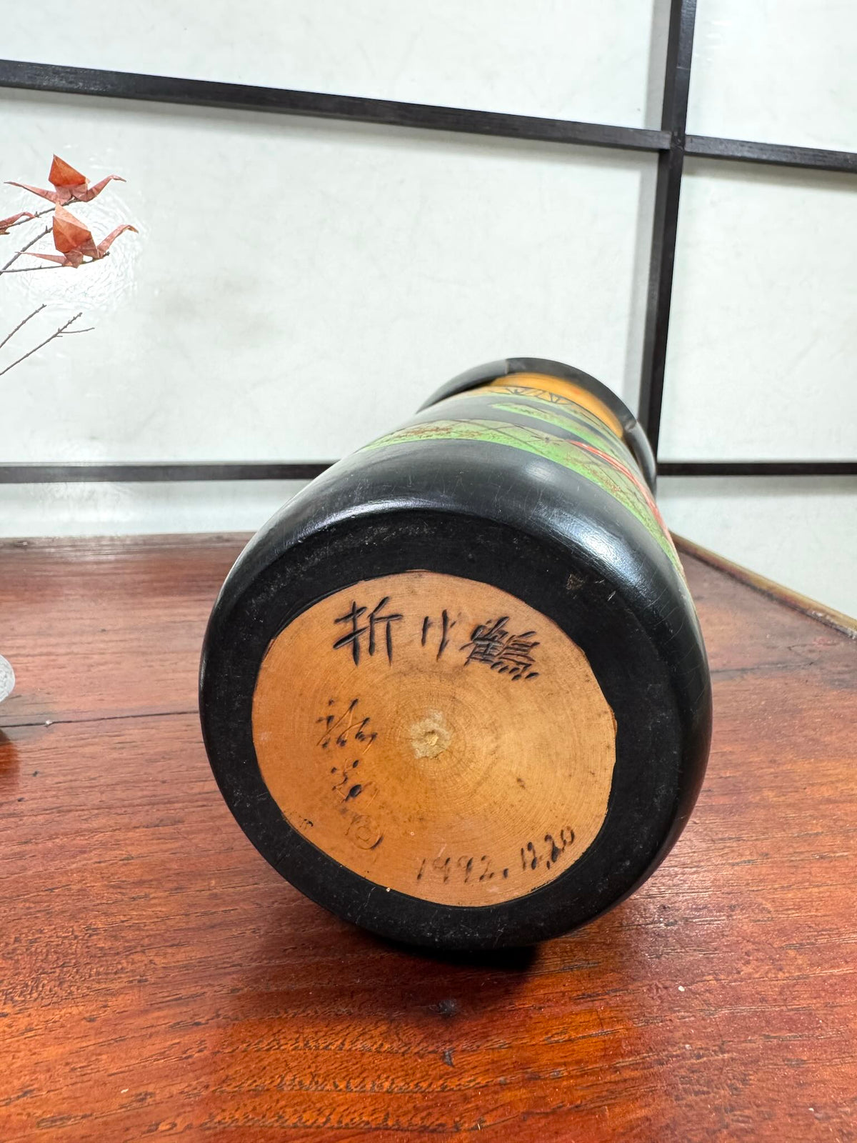 Kokeshi vintage de Yuji Kawase datée de 1992, décorée de grues en origami jaunes et rouges sur un corps noir, le dessous avec signature de l'artiste et date 1992.12.20