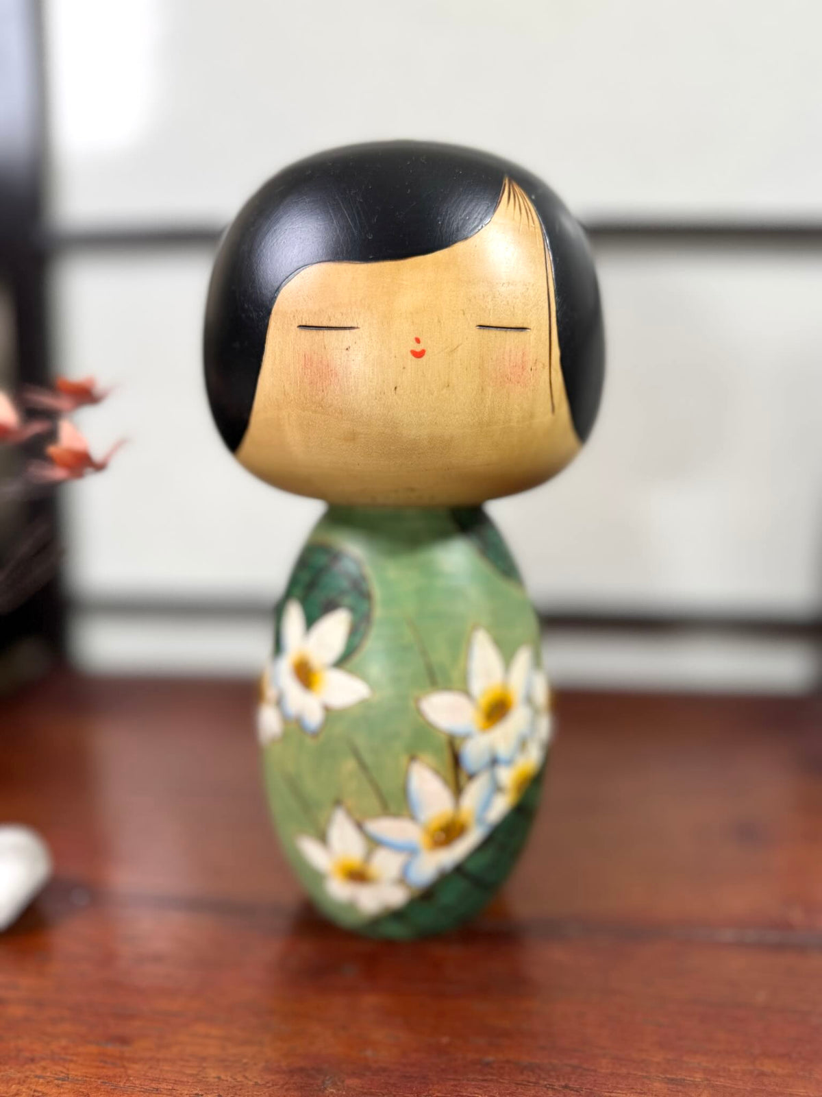 Kokeshi vintage de Yuji Kawase datée de 1994, au corps vert décoré de fleurs blanches et à la coiffure noire asymétrique, portrait