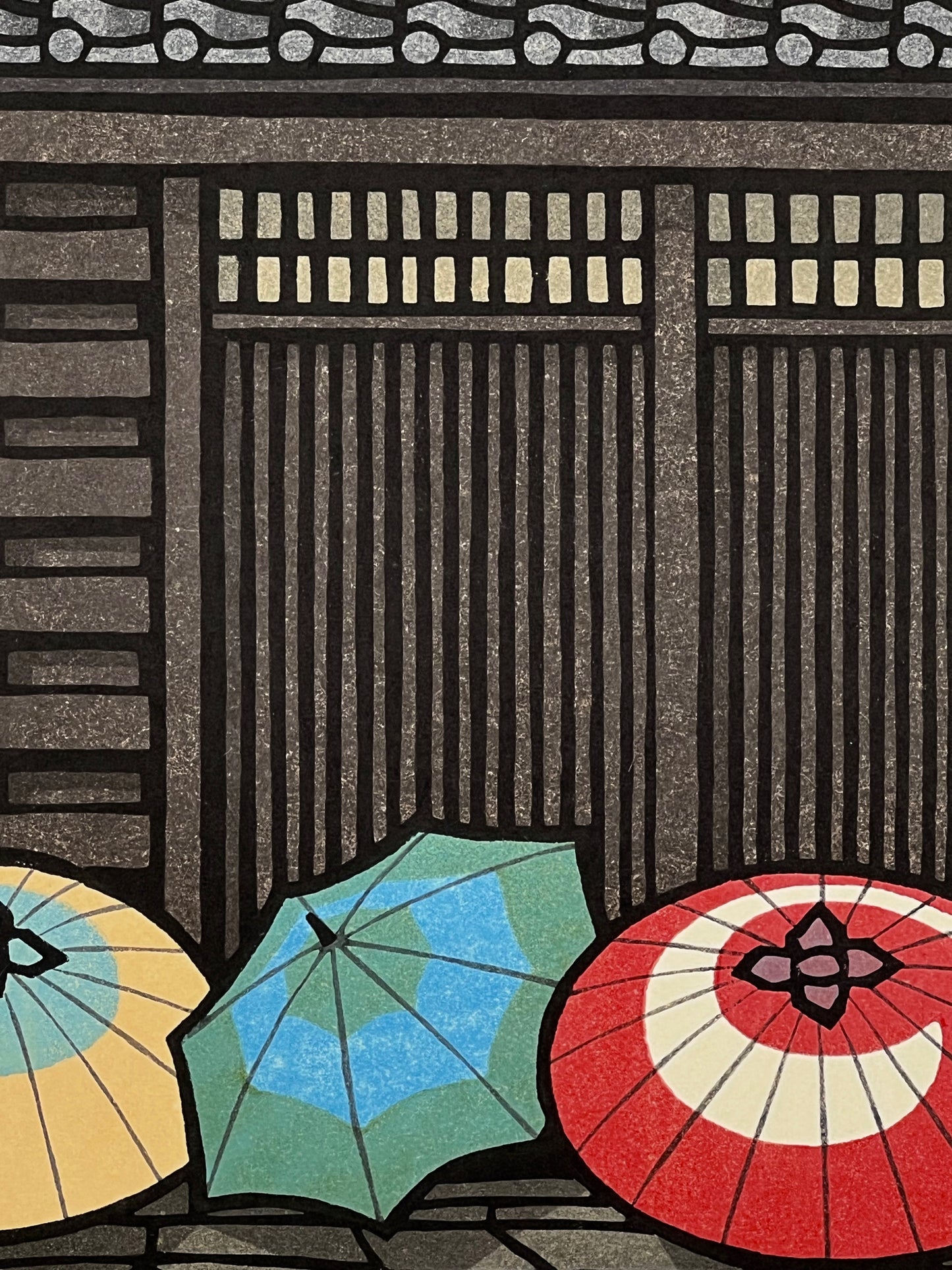 estampe japonaise trois parapluies devant une maison traditionnelle en bois, gros plan sur les parapluies colorés