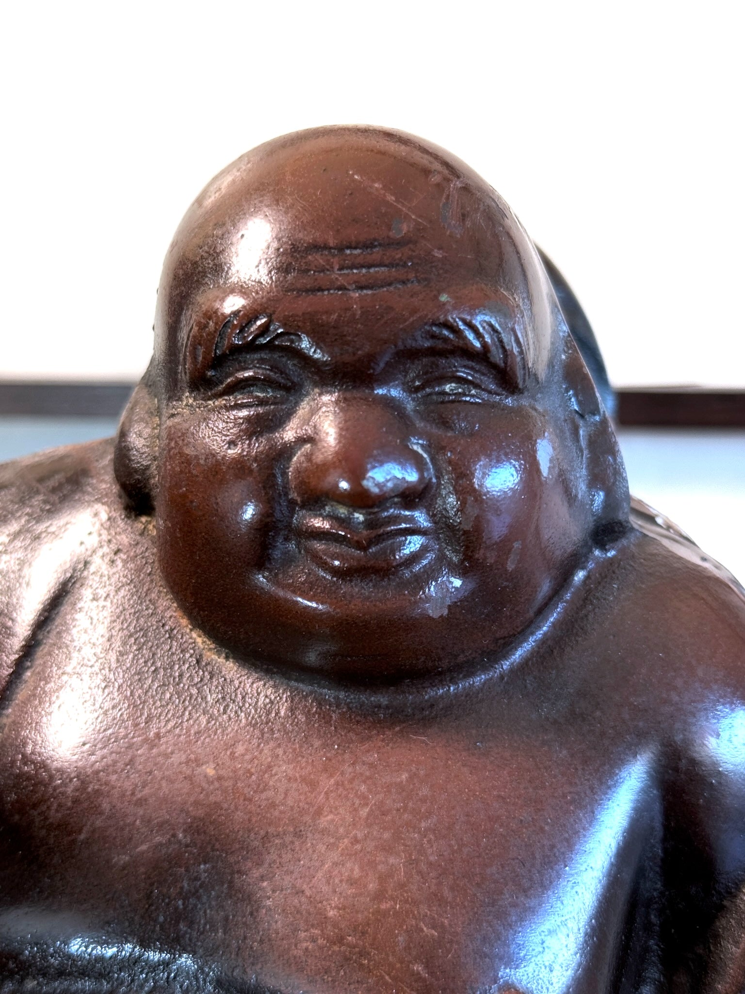 statuette en bronze cuivré de Hotei, dieu du bonheur, gros plan sur le visage souriant