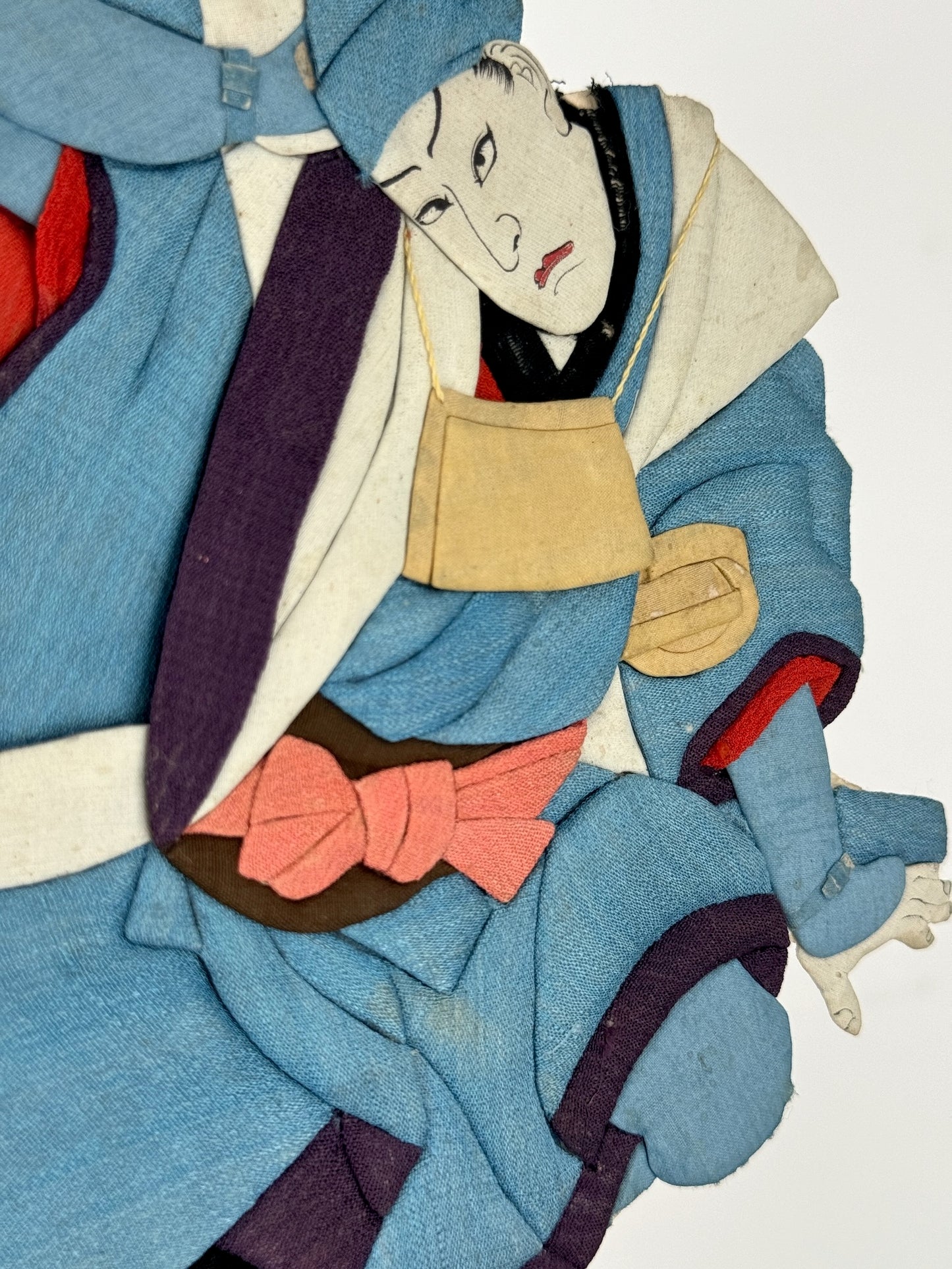 Okiyage japonais représentant un danseur en kimono bleu en tissu, dans une posture dynamique, avec visage peint à la main et accessoires suspendus, profil