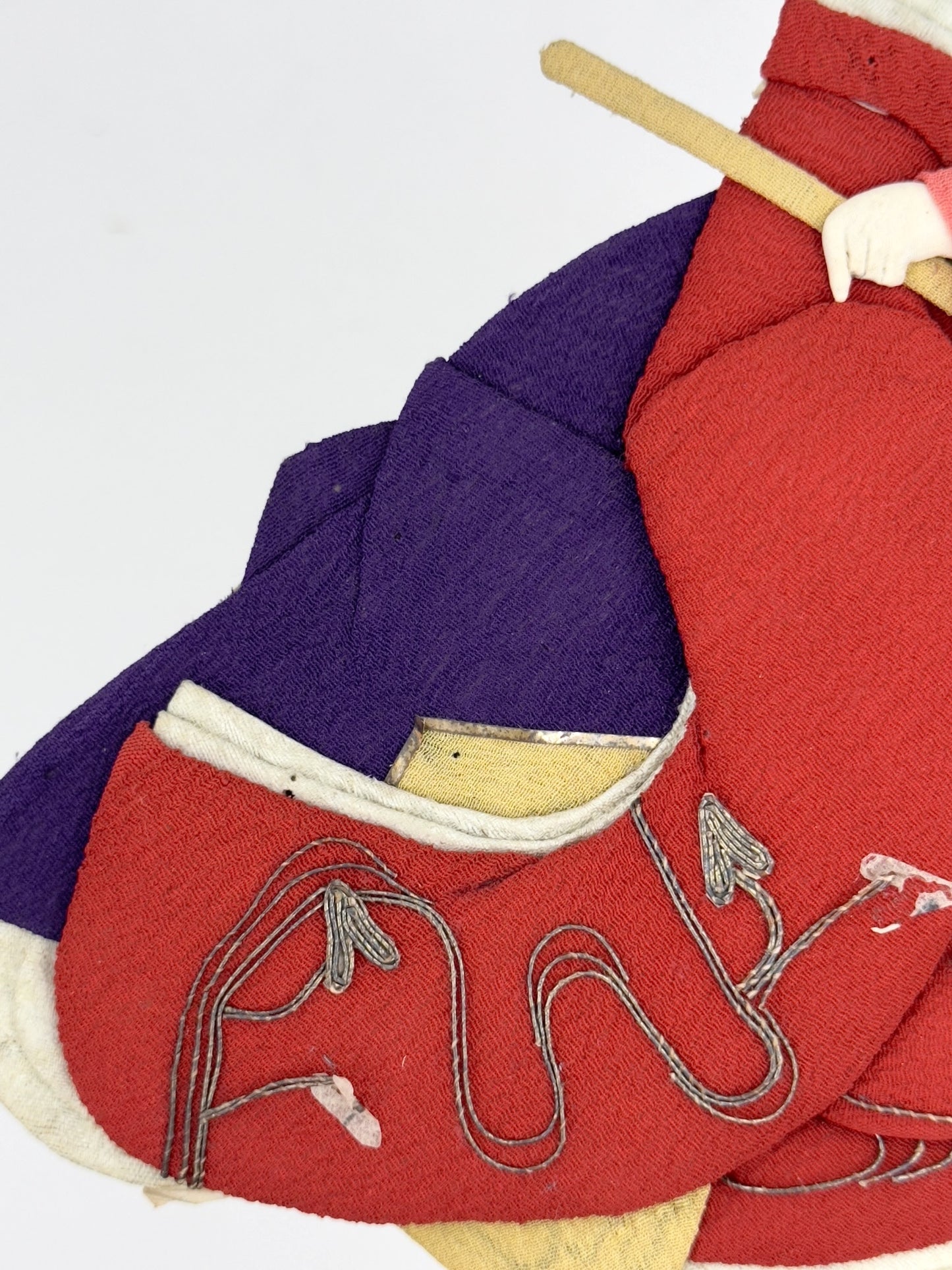 Okiyage japonais représentant une femme jouant du tambour, vêtue d’un kimono rouge brodé, coiffée de fleurs et rubans, réalisée en tissu, gros plan sur la broderie de fils d'argent