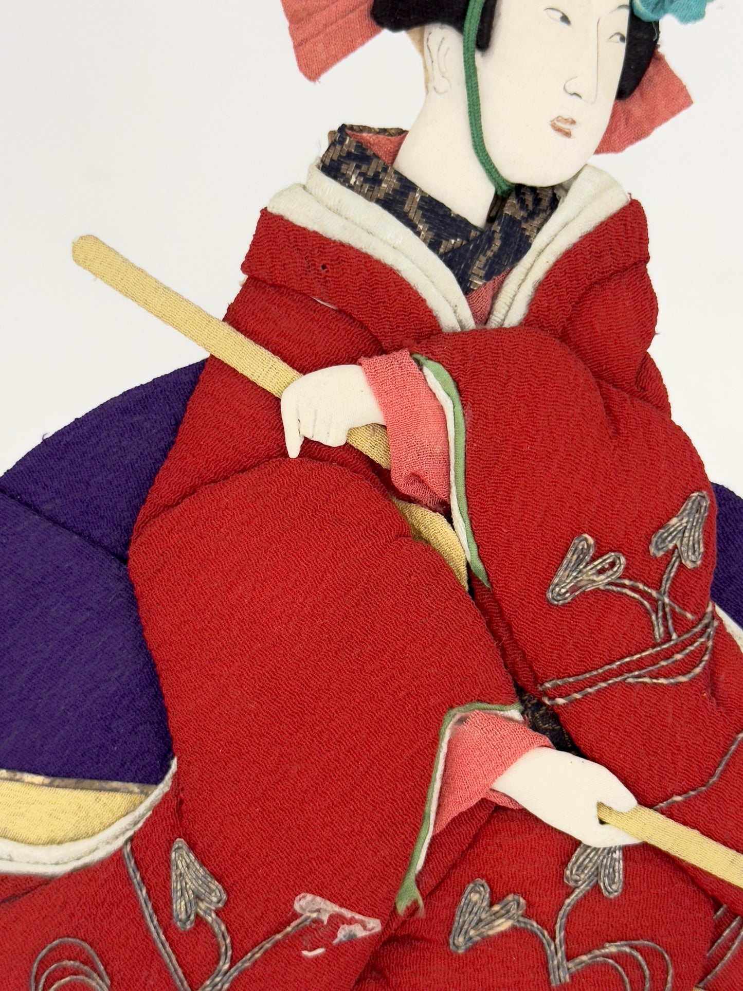 Okiyage japonais représentant une femme jouant du tambour, vêtue d’un kimono rouge brodé, coiffée de fleurs et rubans, réalisée en tissu, gros plan sur les mains tenant les baguettes