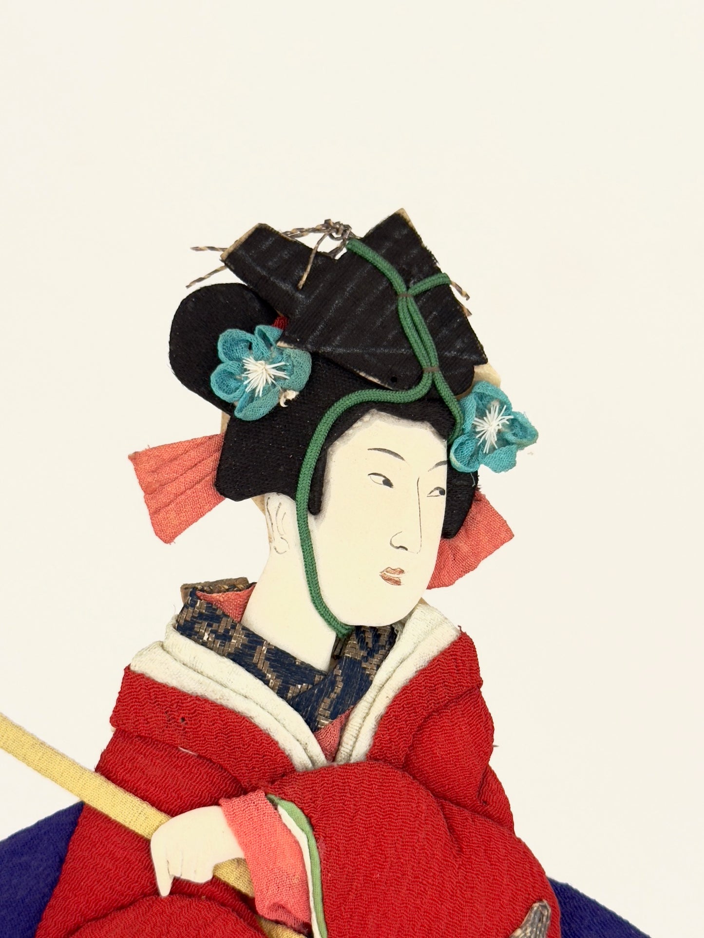 Okiyage japonais représentant une femme jouant du tambour, vêtue d’un kimono rouge brodé, coiffée de fleurs et rubans, réalisée en tissu, gros plan sur le visage