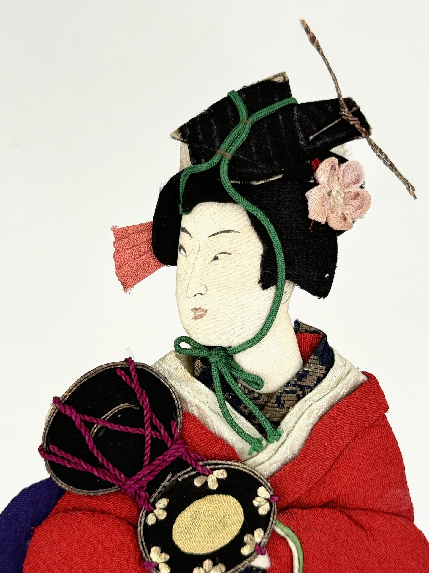 Okiyage japonais représentant une femme en kimono rouge brodé tenant un tambour tsuzumi, réalisée en tissu ancien avec coiffure et accessoires traditionnels, gros plan sur le visage.