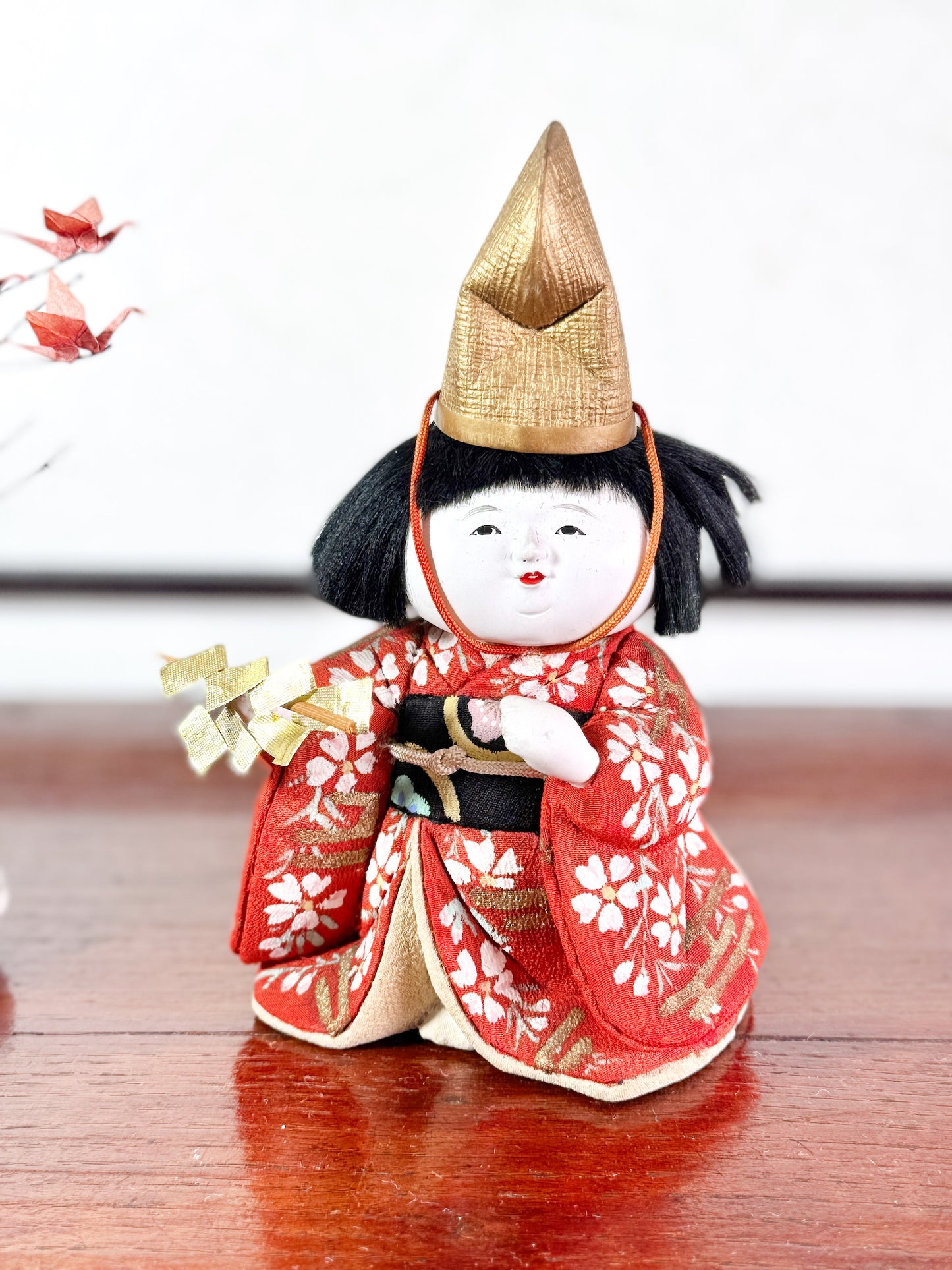 Poupée japonaise Kimekomi en kimono rouge avec chapeau doré et bâton rituel shintō, vu de face.