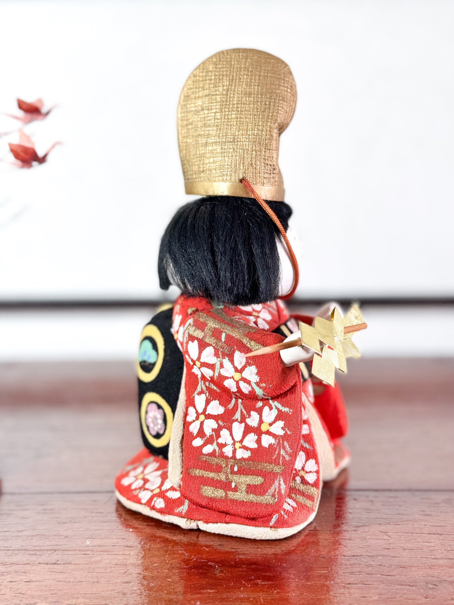 Poupée japonaise Kimekomi en kimono rouge avec chapeau doré et bâton rituel shintō, vu du profil droit