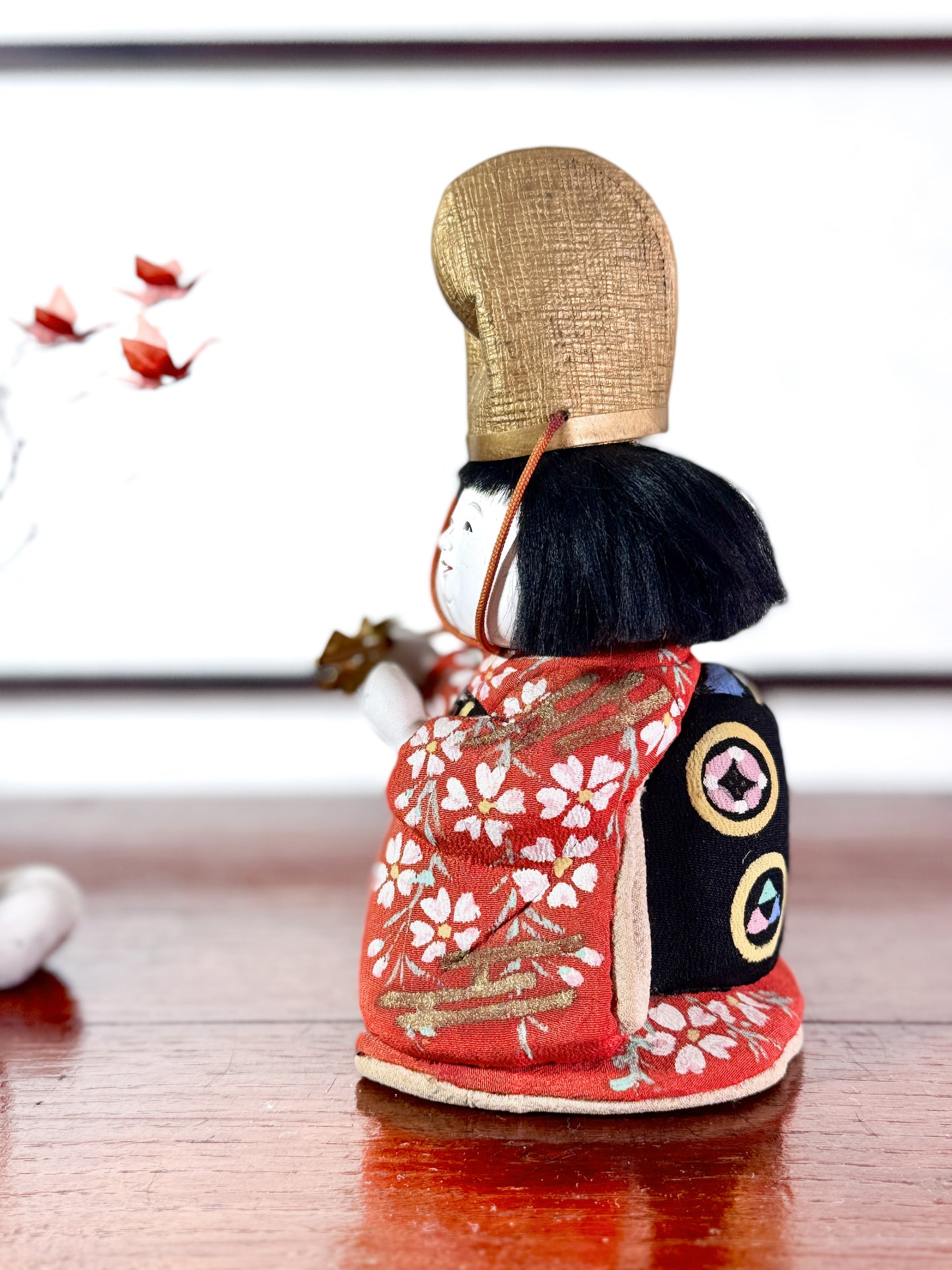 Poupée japonaise Kimekomi en kimono rouge avec chapeau doré et bâton rituel shintō, vu du profil gauche